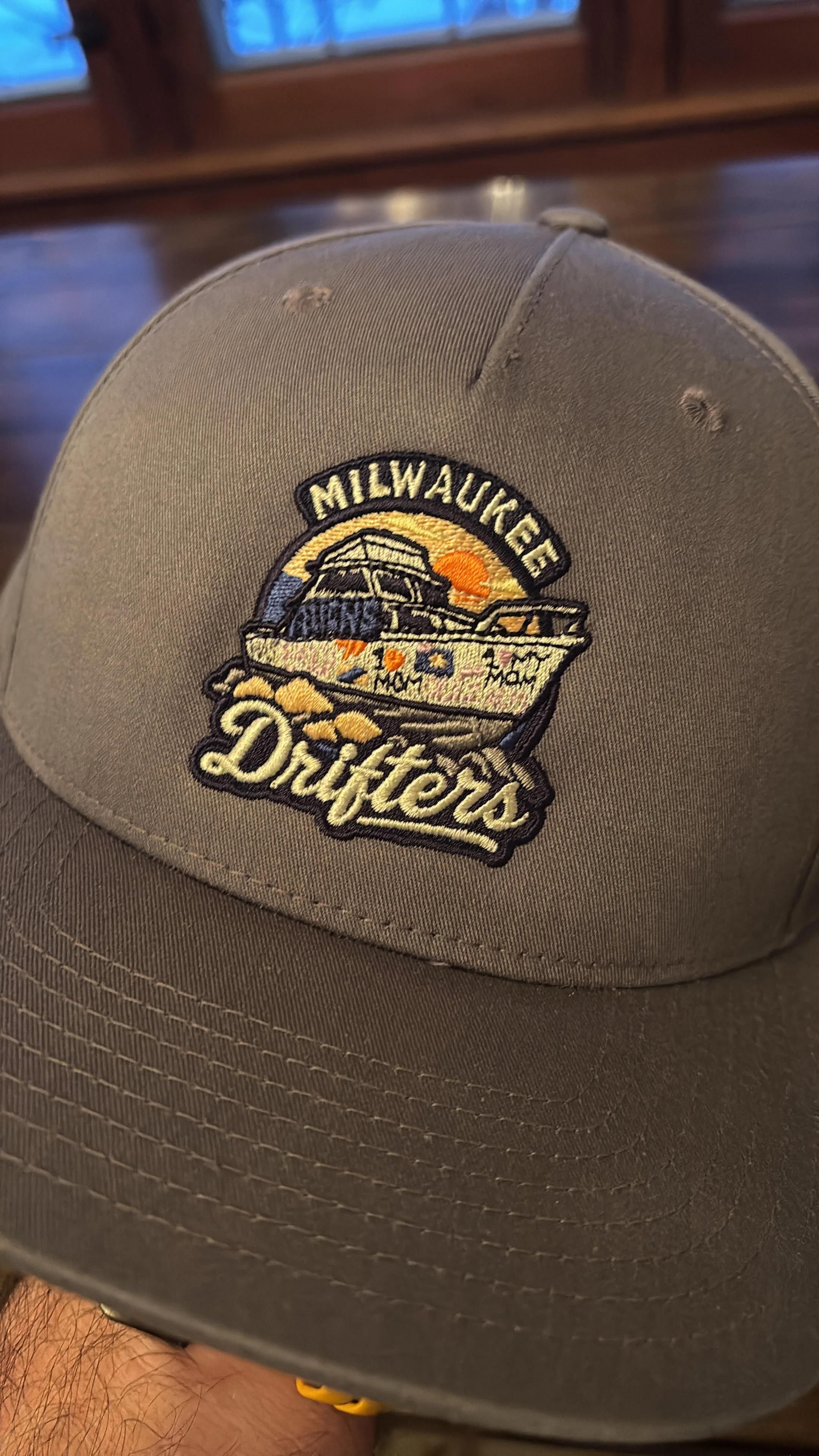 Gray baseball cap with an embroidered patch of a boat, sunset, and the words 'Milwaukee Drifters' on the cap. This is designed to be a logo hat for a softball team.