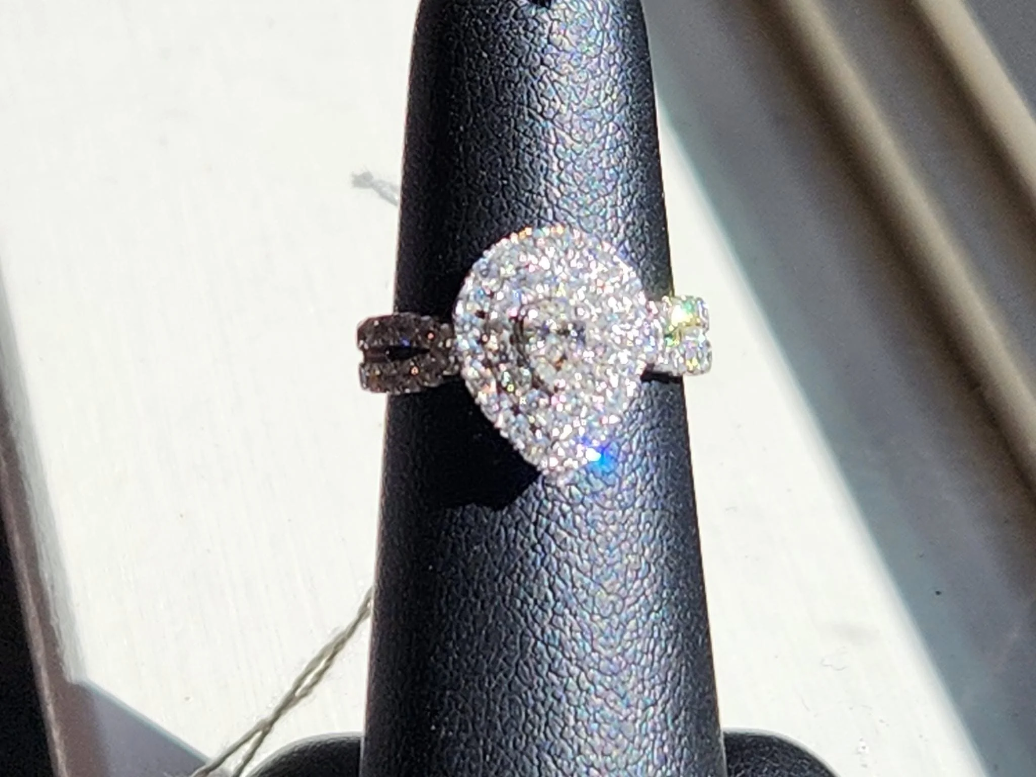 Close-up of a sparkly diamond ring with a heart-shaped center, set on a black display stand.