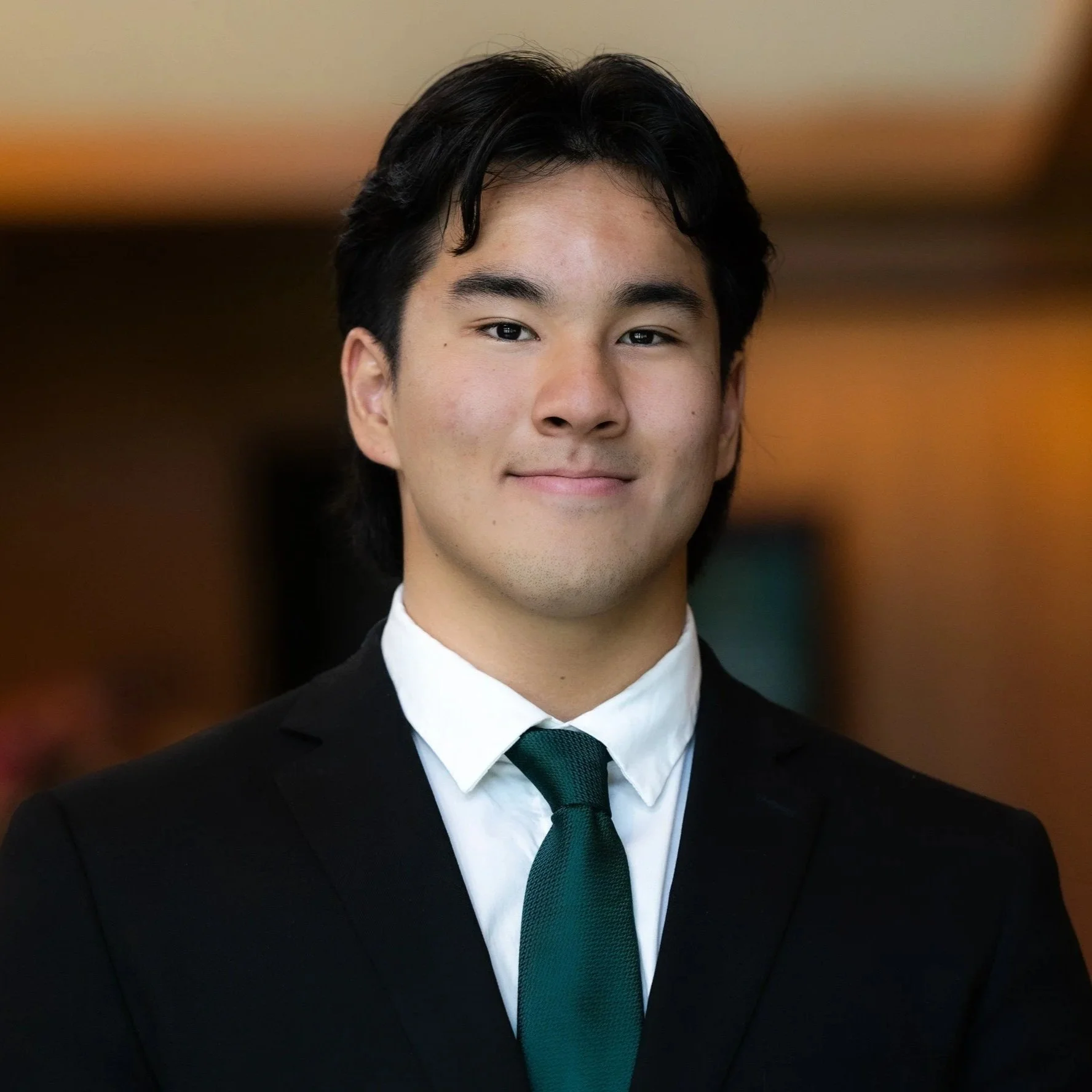 Young man in a suit and tie smiling in a professional setting.