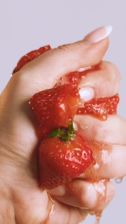 Close-up of a hand squeezing ripe strawberries, causing juices to drip.