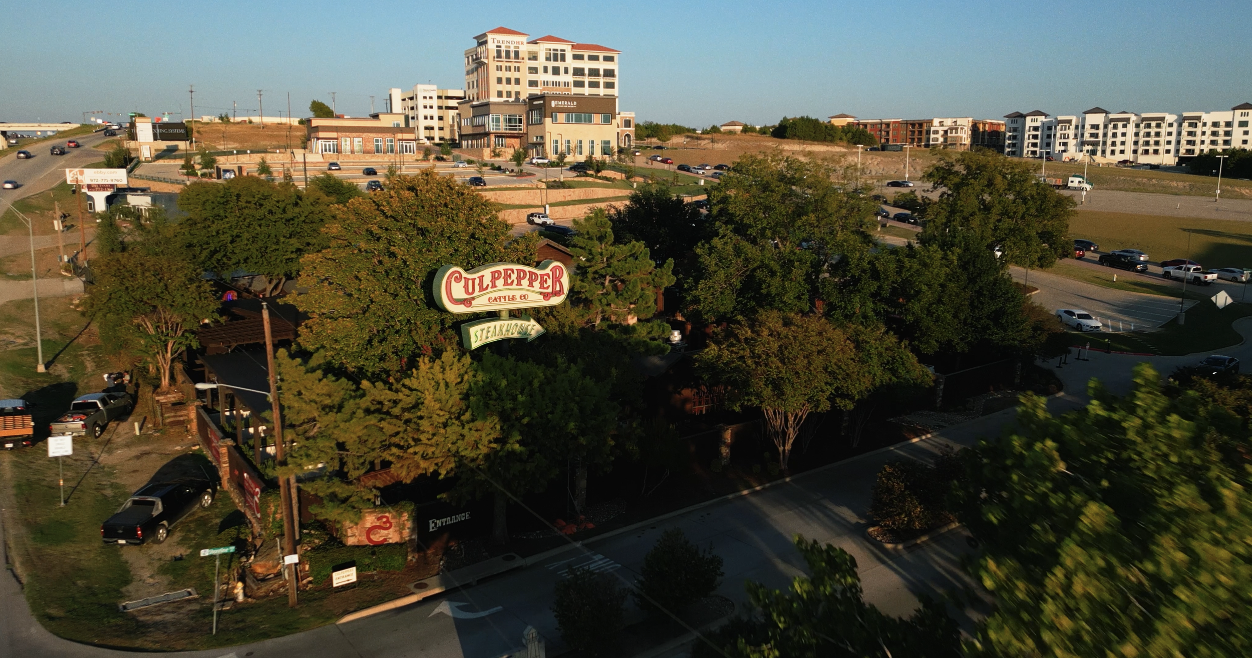 Aerial view of Culpepper Steak House, surrounded by trees, with parking lot and city buildings in the background, during daytime.