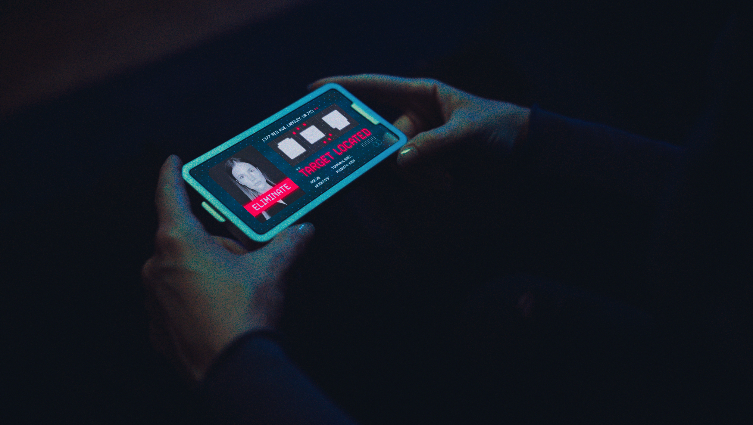 A person holding a smartphone with a futuristic security or surveillance interface on the screen, showing a woman's photo, a digital countdown timer, an option to eliminate the target, and the message 'TARGET LOCATED'.