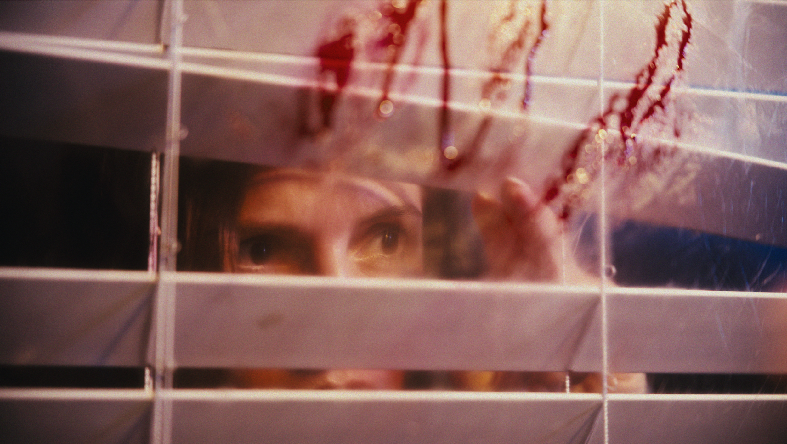 A person peering through window blinds with blood splattered on the glass