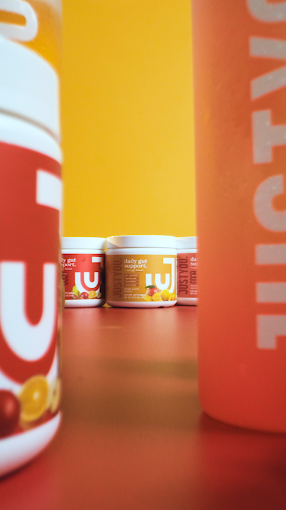 Multiple containers of dietary supplement products with orange and red labels, placed on a red surface against a yellow background.