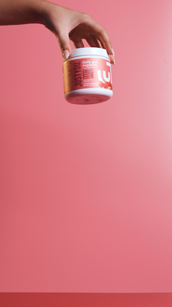 A hand holding a pink container of daily gut support supplement against a pink background.