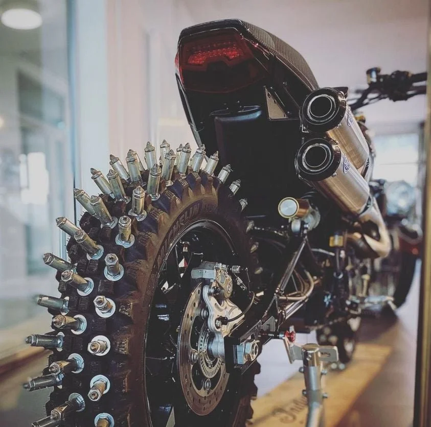 Moto avec pneus cloutés et échappement double en acier inoxydable.