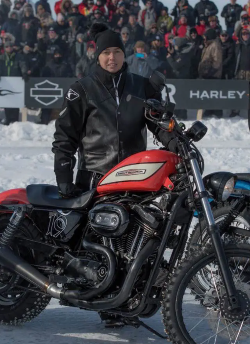 Une femme habillée en veste noire et bonnet, posant avec une moto dans un environnement enneigé devant une foule
