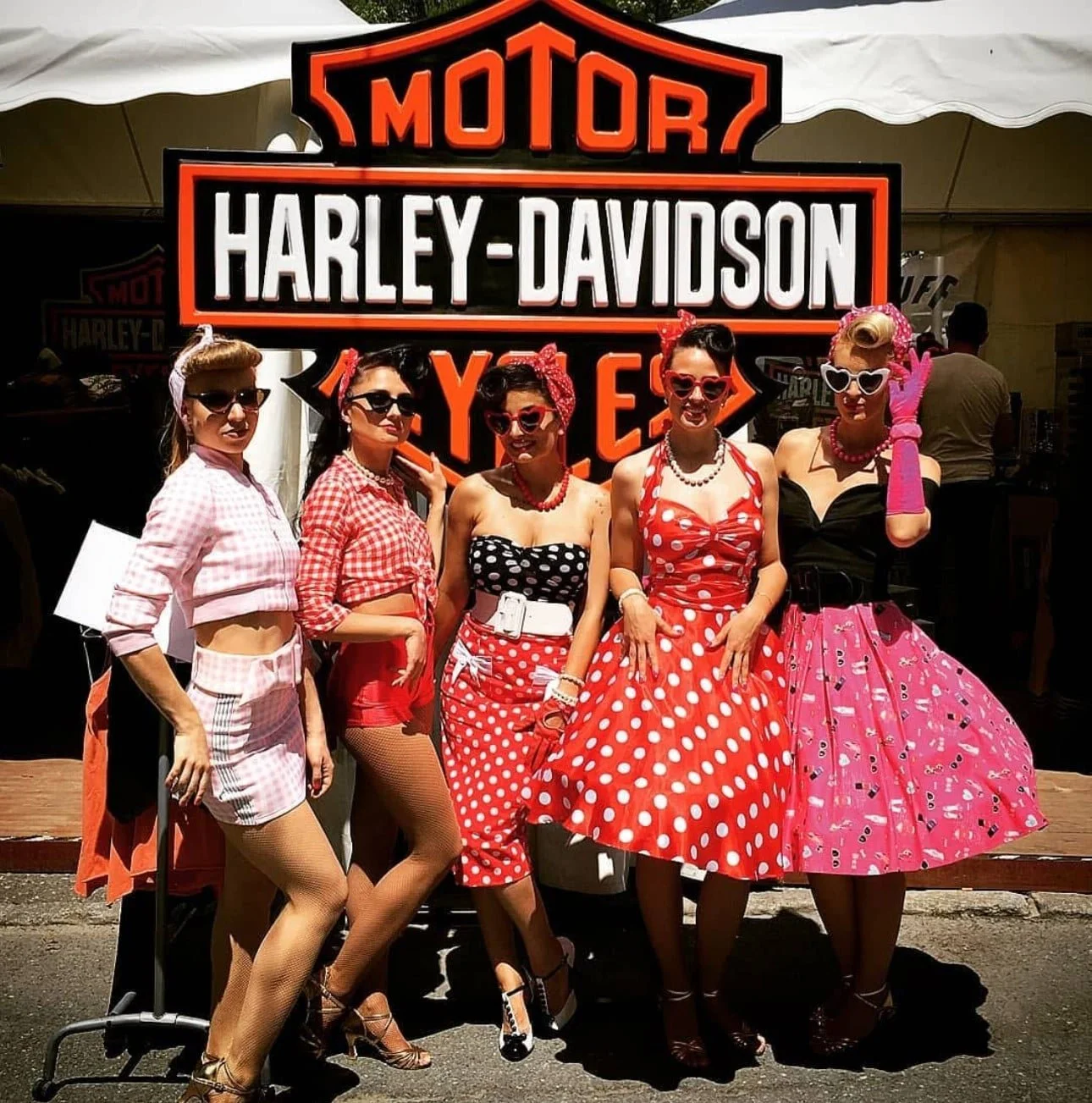 Un groupe de femmes habillées dans un style vintage pin-up devant un panneau lumineux Harley-Davidson.