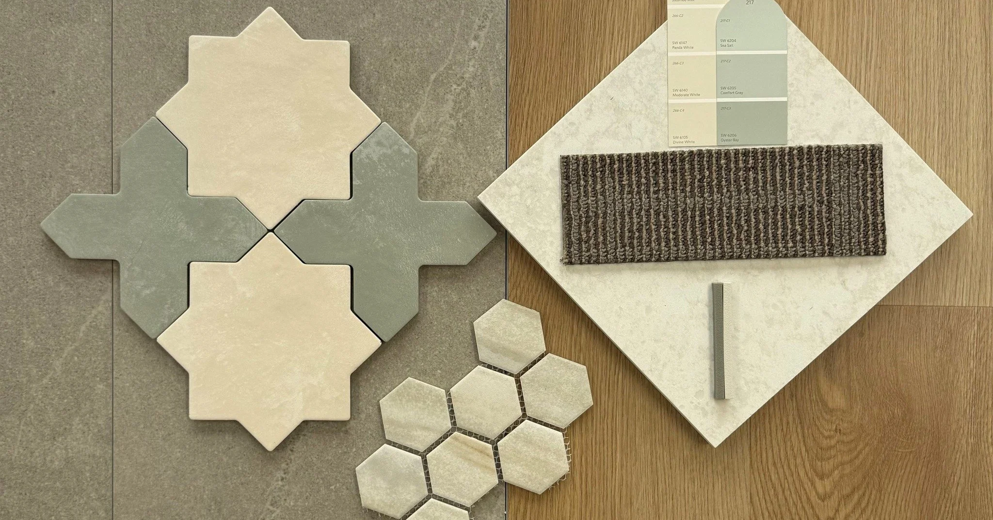 A collection of tile samples, including large geometric-shaped tiles, smaller hexagonal tiles, and color swatches, arranged on a wooden surface.