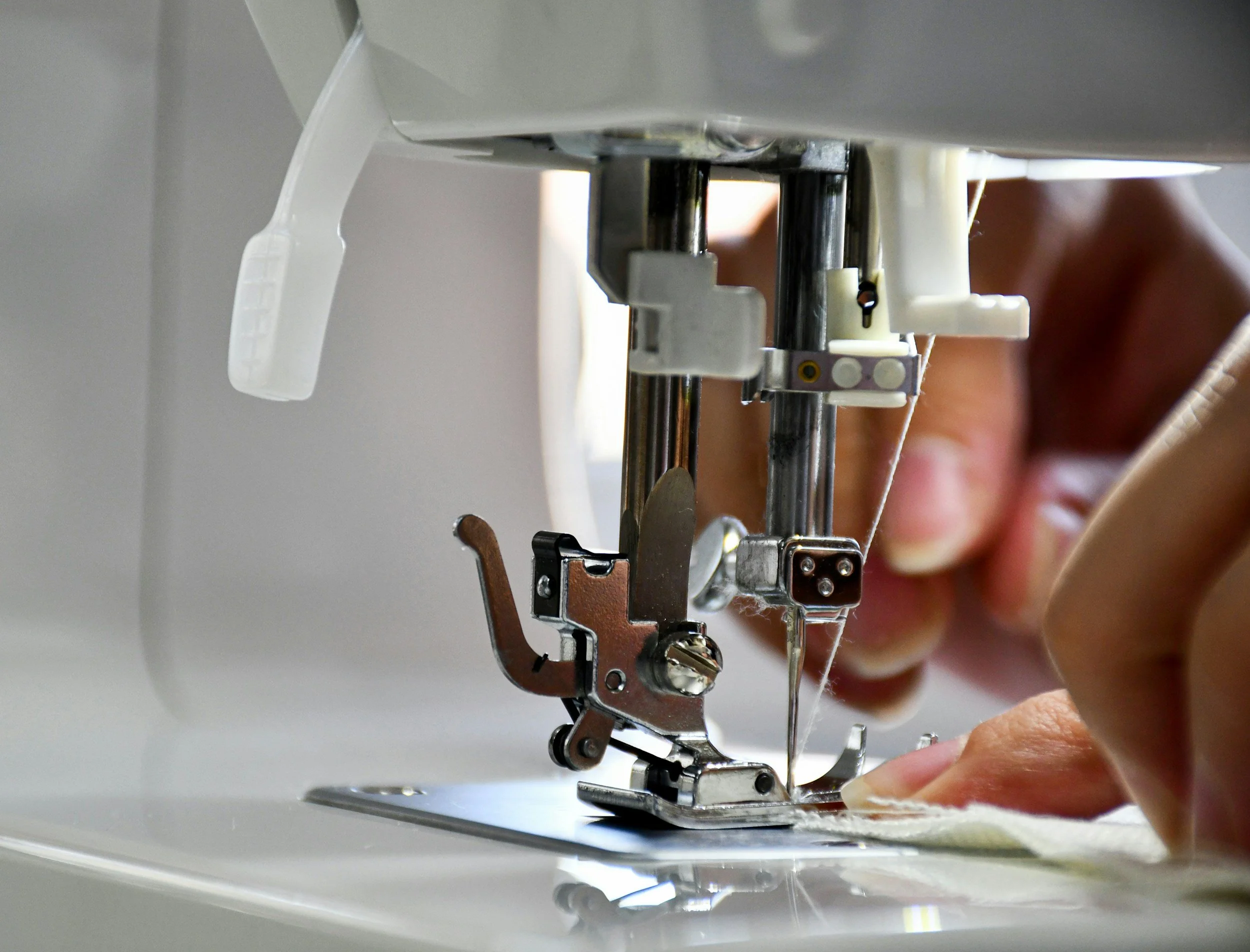 Close-up of a person's hand guiding fabric through a sewing machine needle and presser foot.