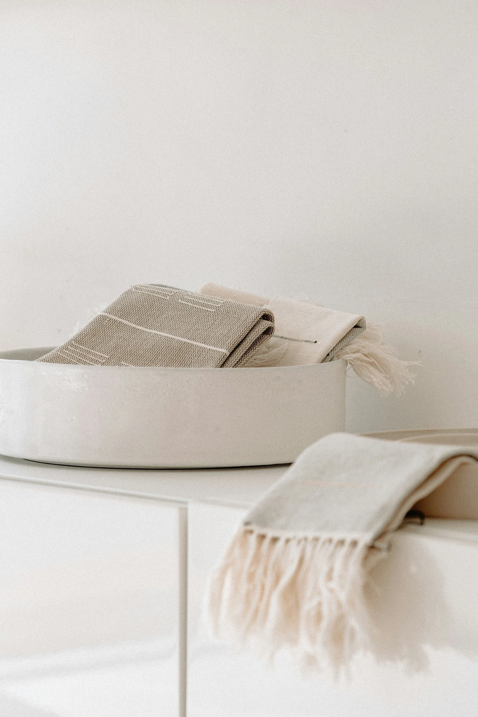 Stack of neutral-colored textiles and towels on a white surface with a plain background.