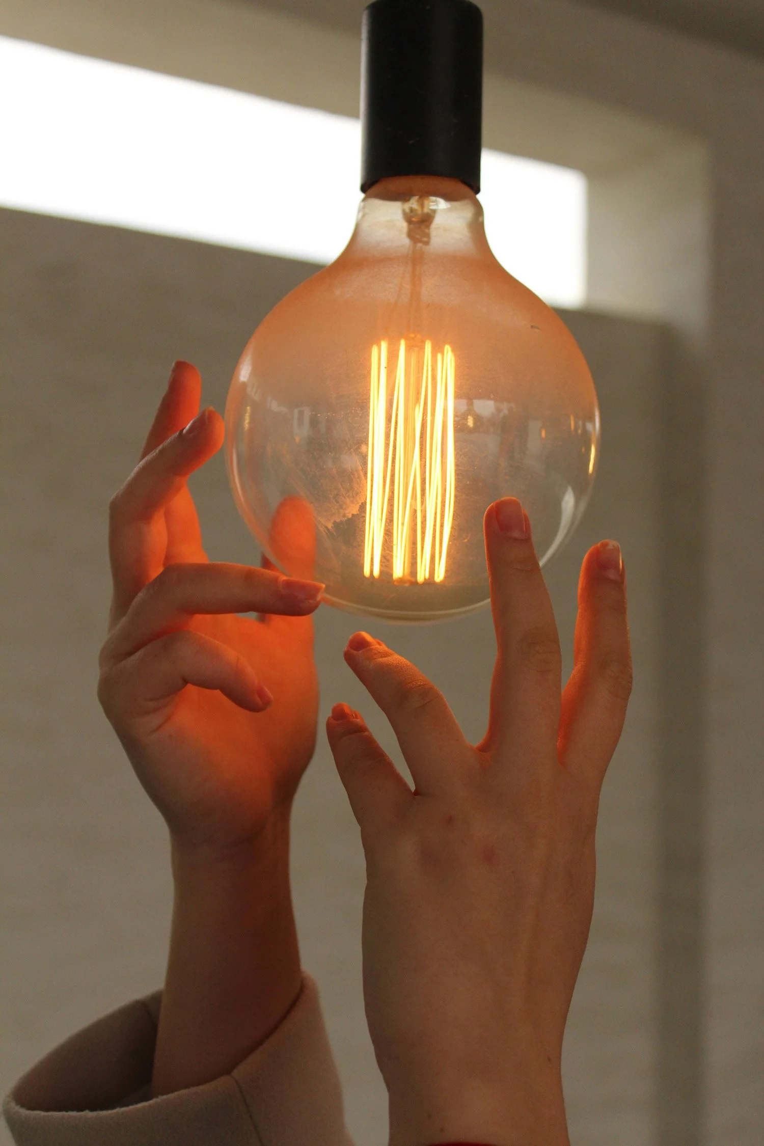 A person holding a glowing Edison-style light bulb with their hands, against a blurred background.