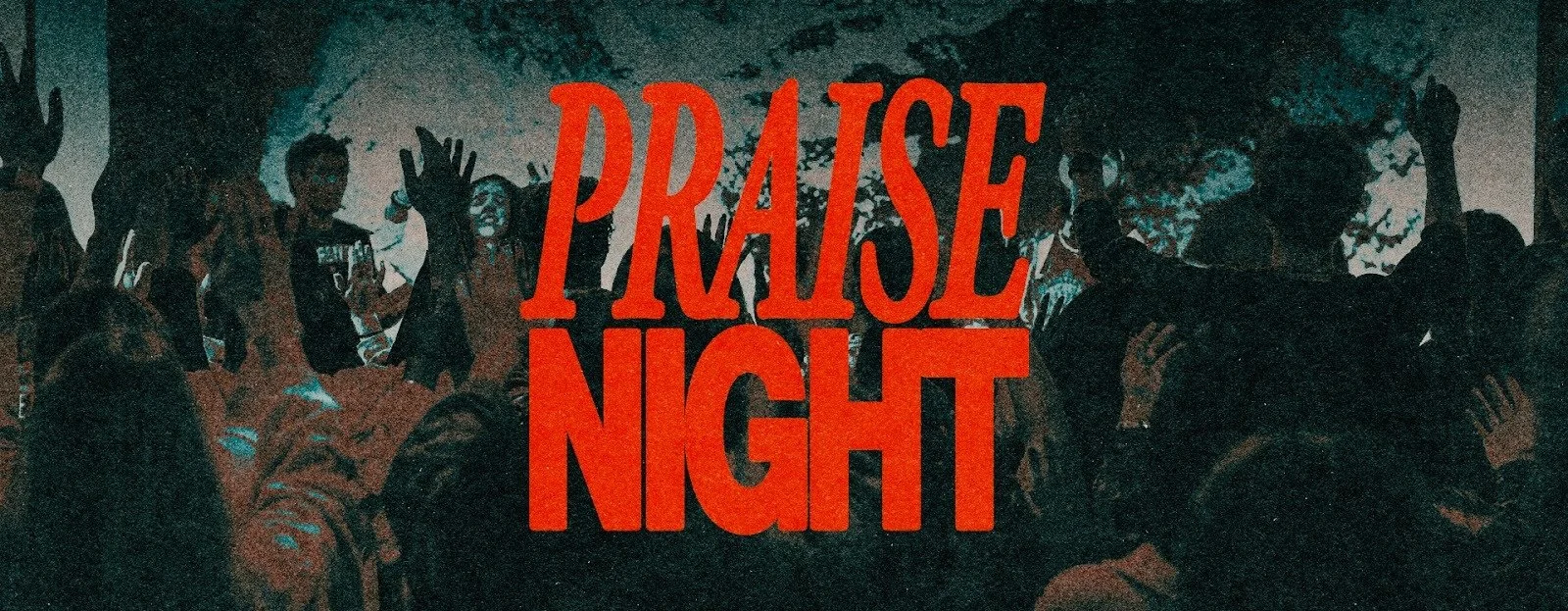 Crowd of people at a prayer night event, with some raising their hands, and a woman speaking or singing into a microphone on the stage.