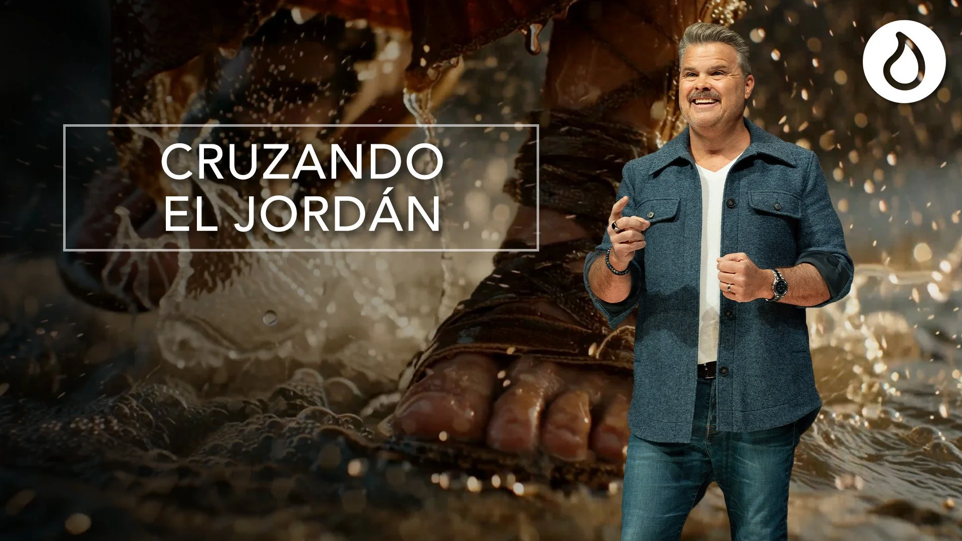 A man in a blue jacket and jeans smiling, standing in front of a background of a large crocodile submerged in water with its head and part of its body above the surface. The text 'Cruzando el Jordán' overlays the image.