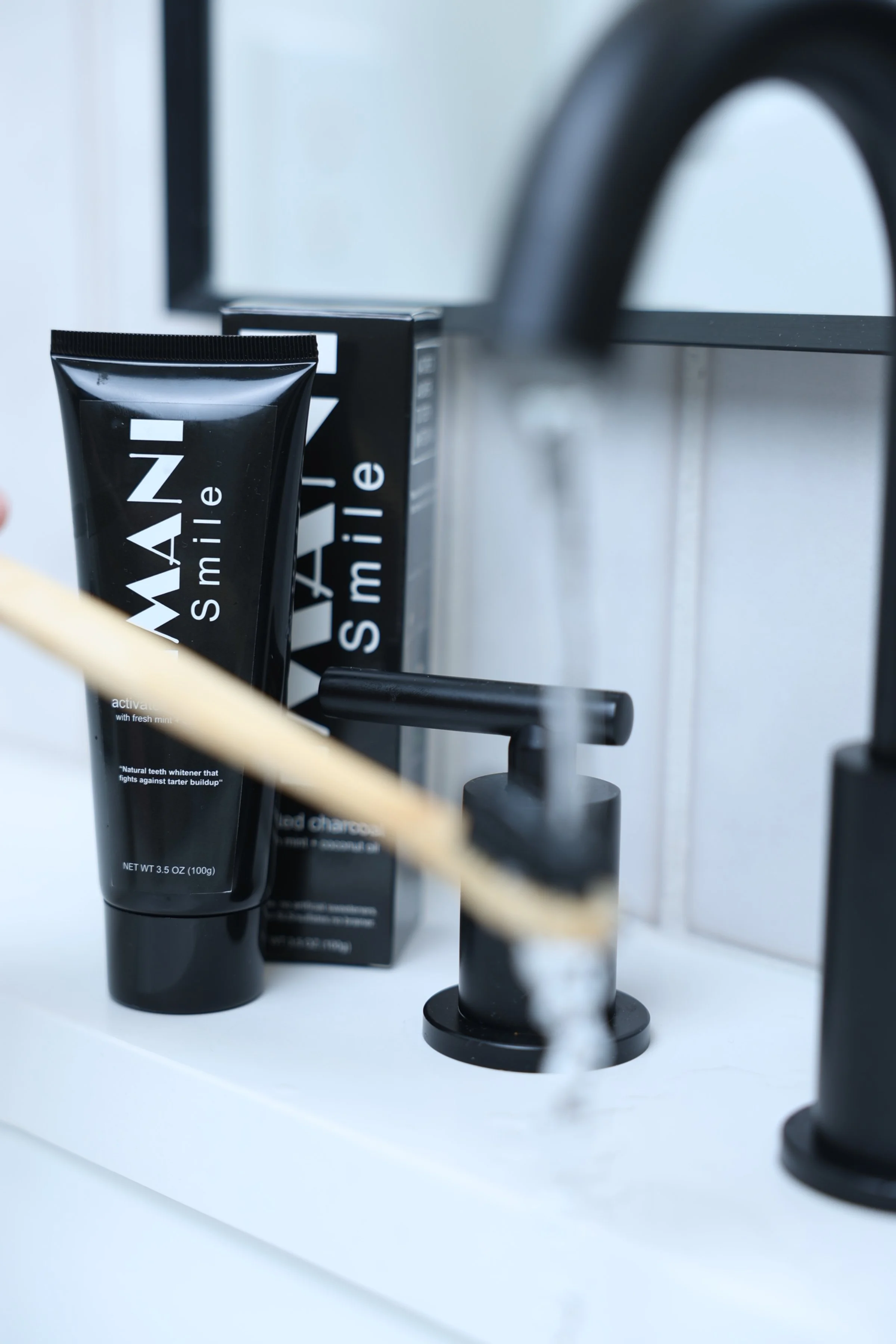 A black tube of toothpaste labeled 'MAN Smile,' a black soap dispenser, and a black box of toothpaste on a white bathroom counter, with a mirror in the background.