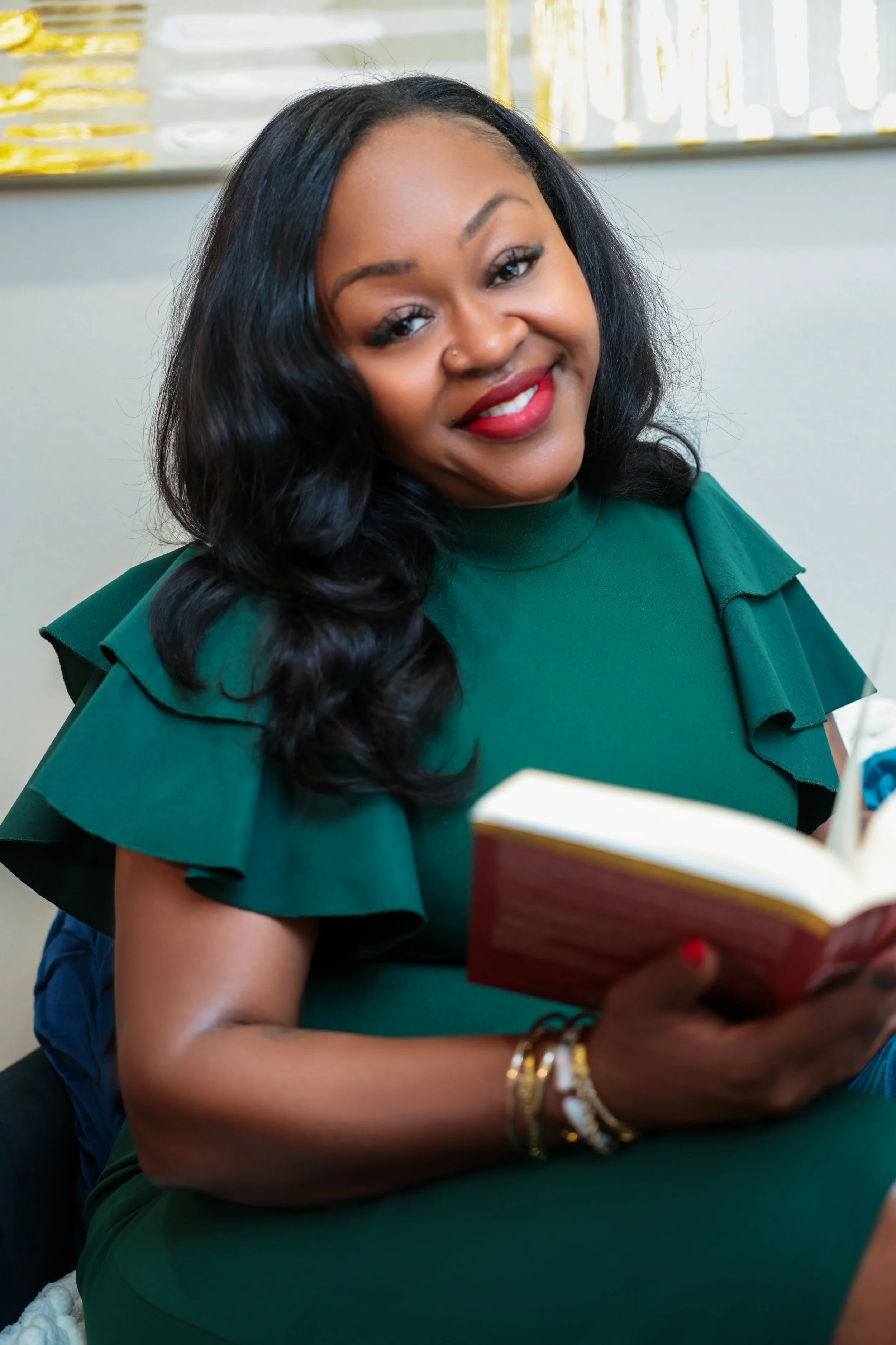 A beige ceramic vase with a narrow neck and wide base, containing dried brown stems with small round seed heads, placed on a wooden surface with a plain light-colored wall behind.