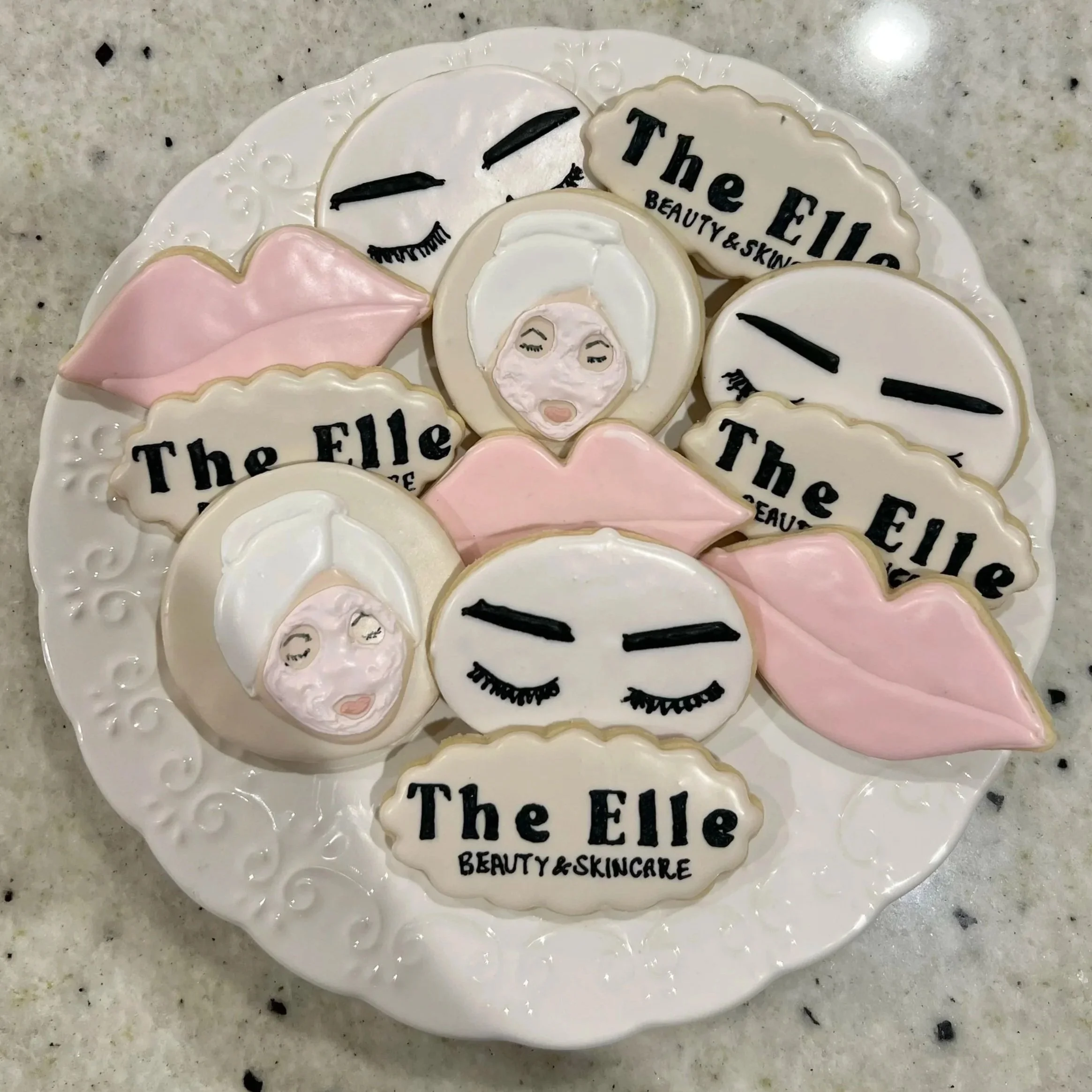 Decorative cookies on a white plate with branding, including facial expressions, lips, eyebrows, and logos for 'The Elle Beauty & Skincare' salon.
