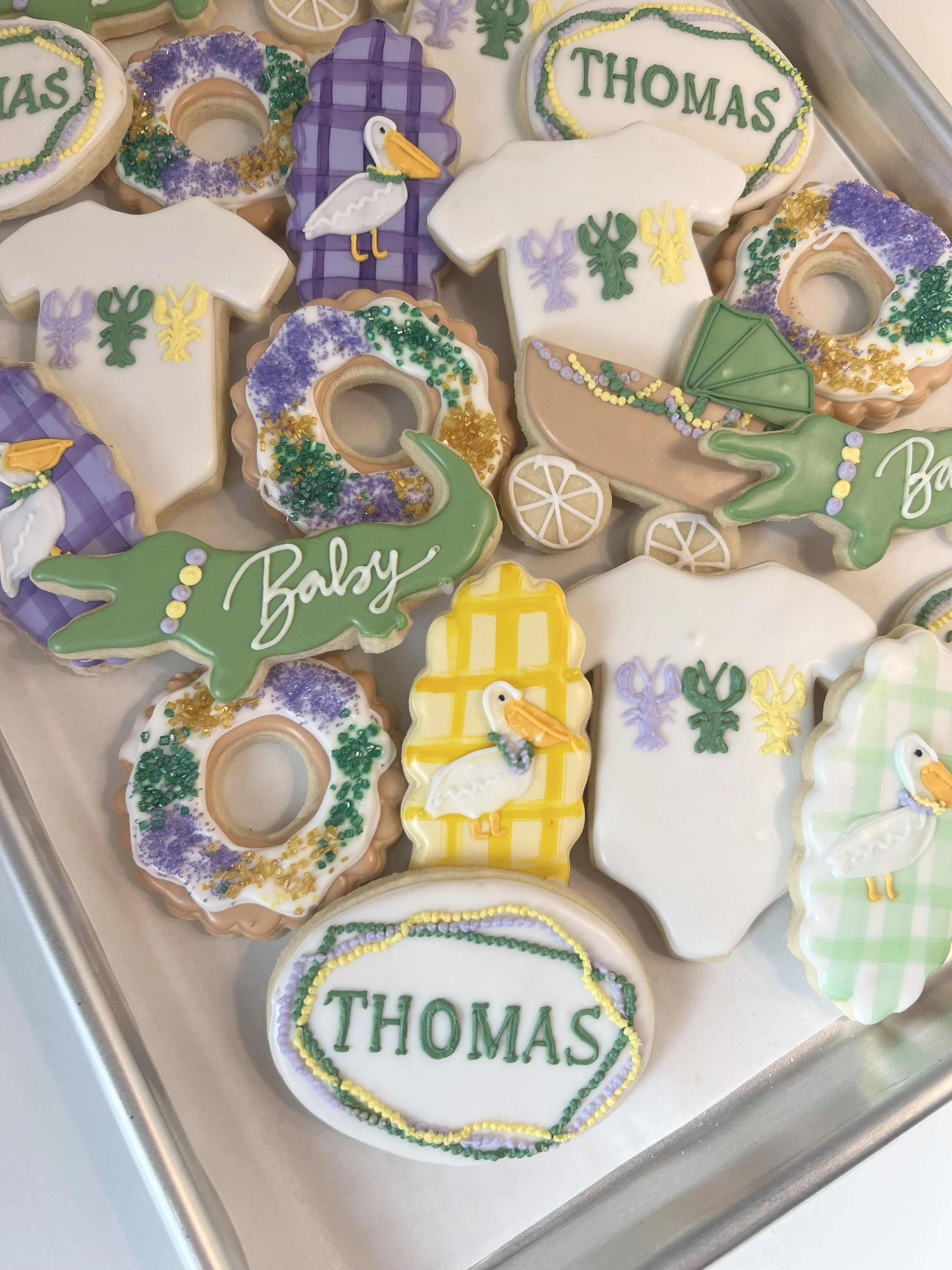 Assorted themed cookies with stork and baby designs, decorated in purple, yellow, green, and white icing, some with the name 'Thomas' written on them.