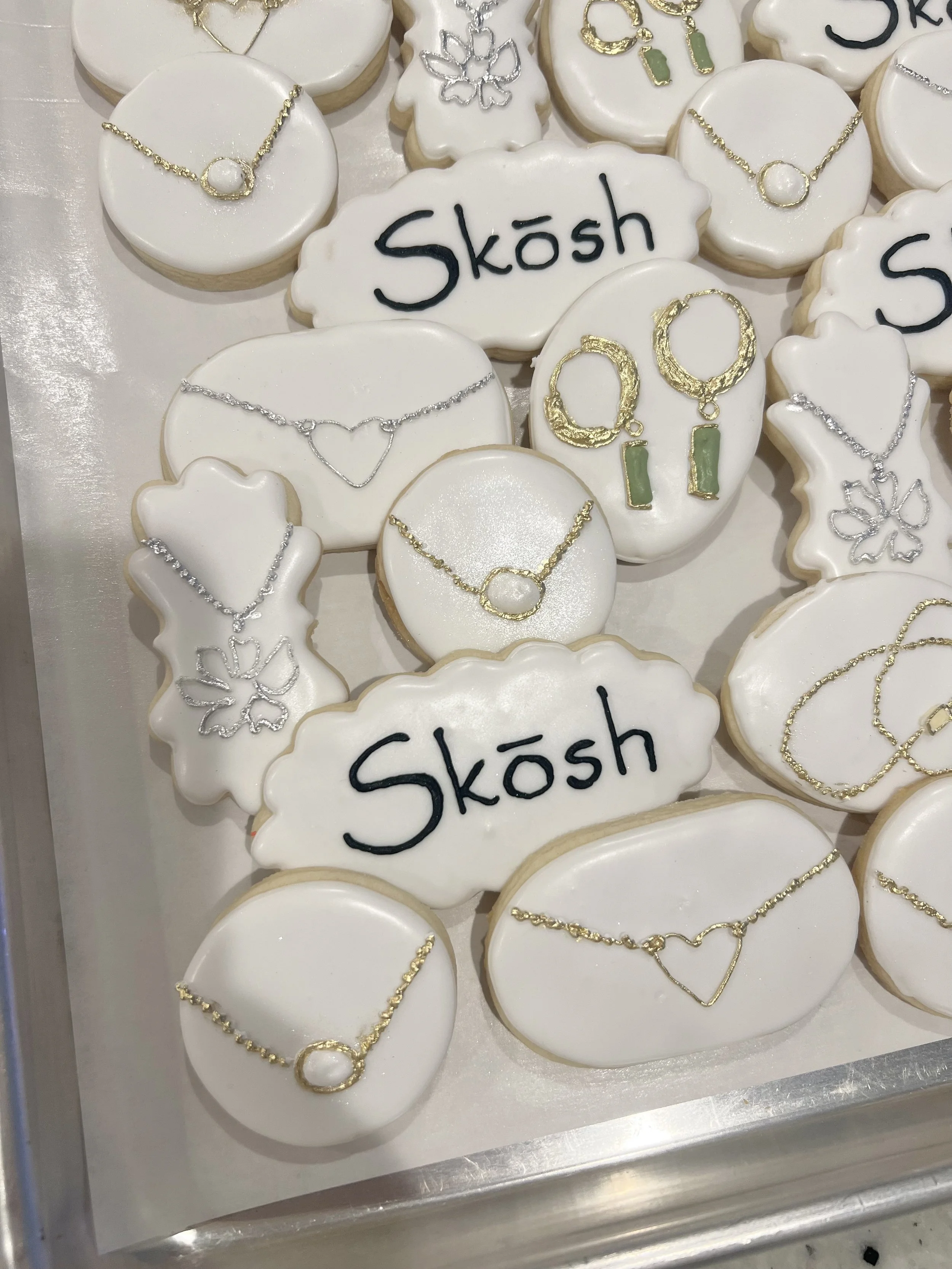 Cookies decorated with jewelry designs and the word 'Skosh' in black icing.