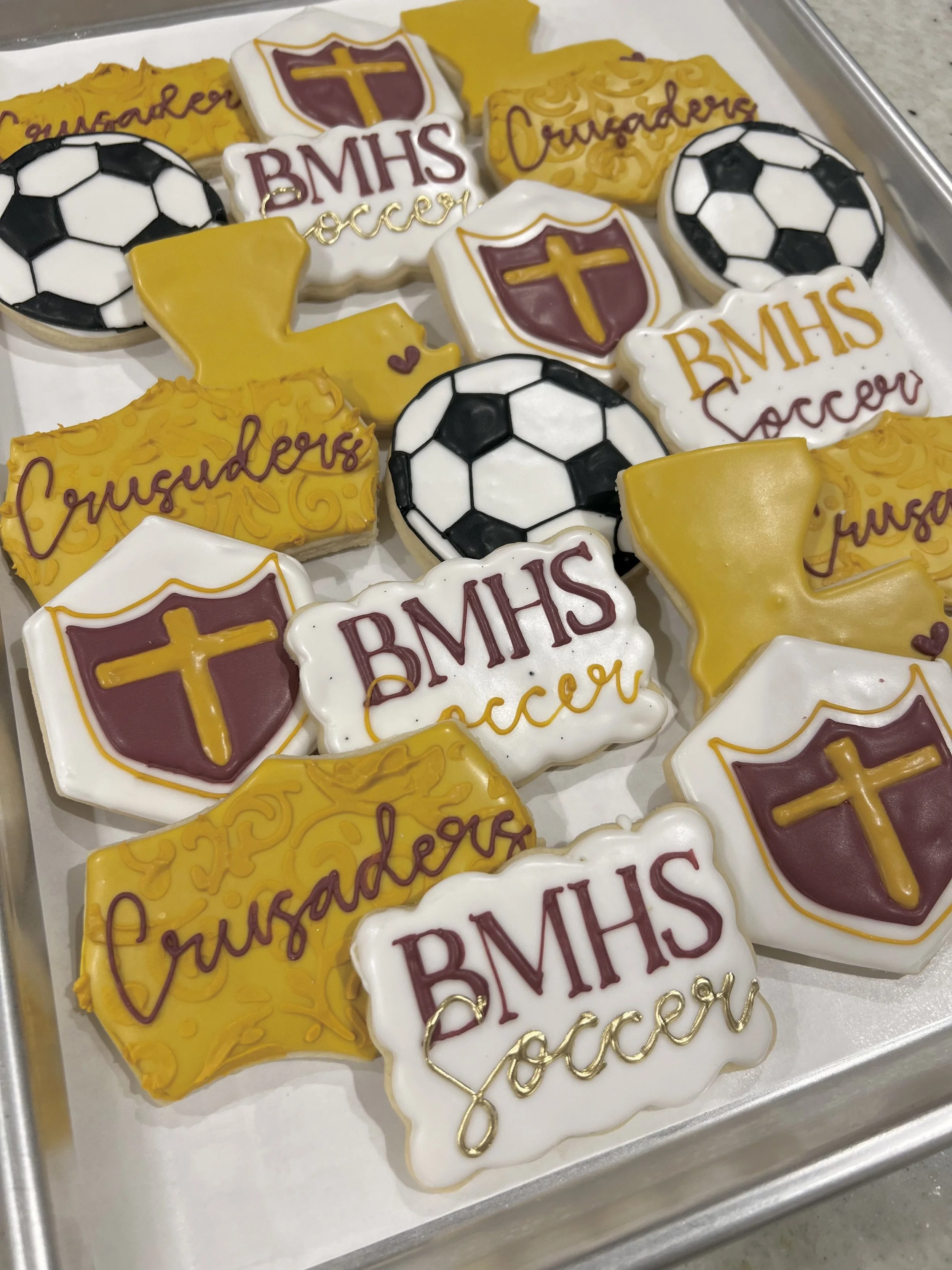 Brother Martin decorated sugar cookies with school and soccer themes, including the words "Crusaders," "BMHS soccer," yellow state shape, soccer ball designs, and school crest symbols.