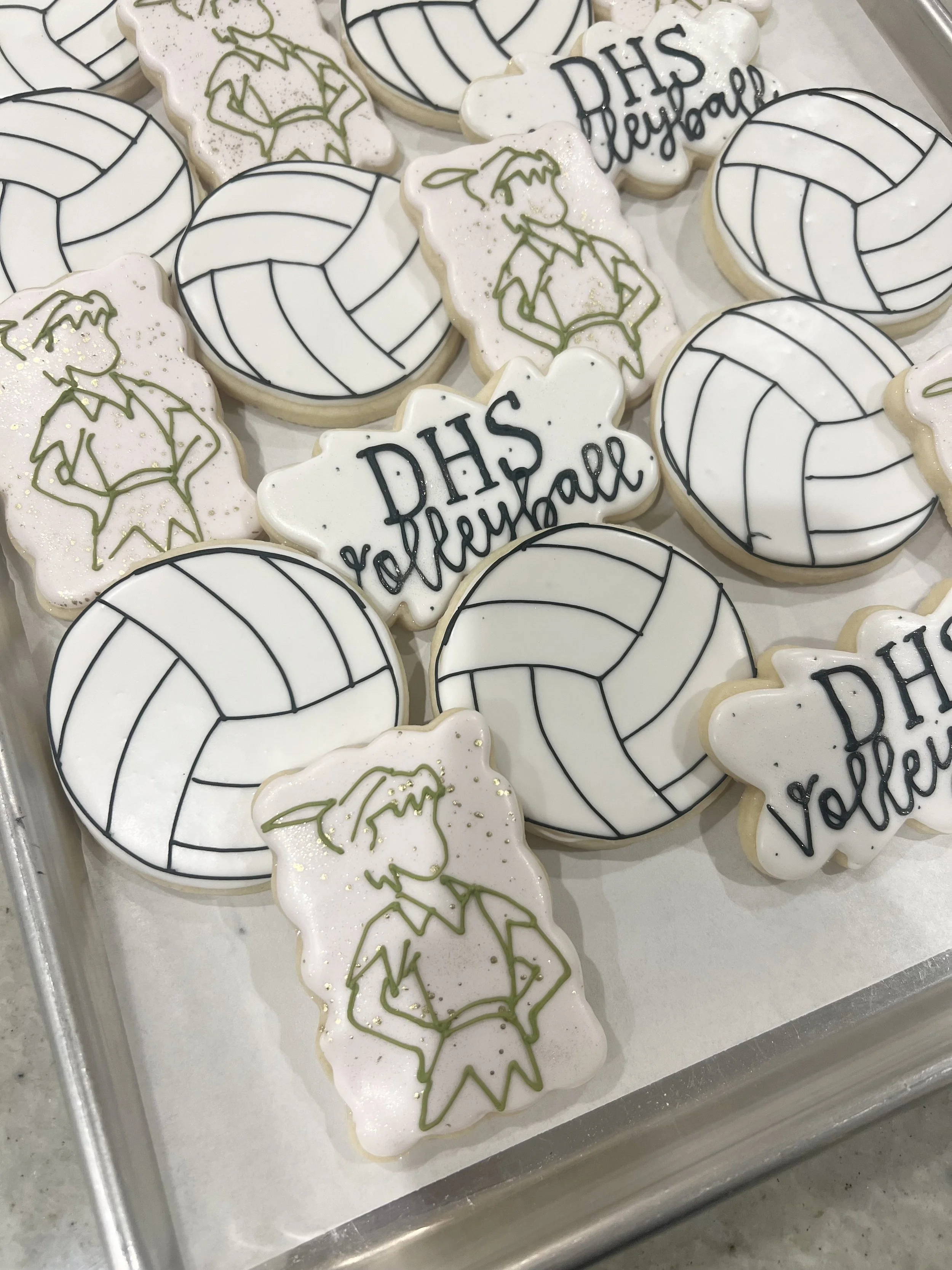 Dominican High School themed cookies decorated with volleyball, a girl with a ponytail, and the phrase "DHS Volleyball" in black icing.