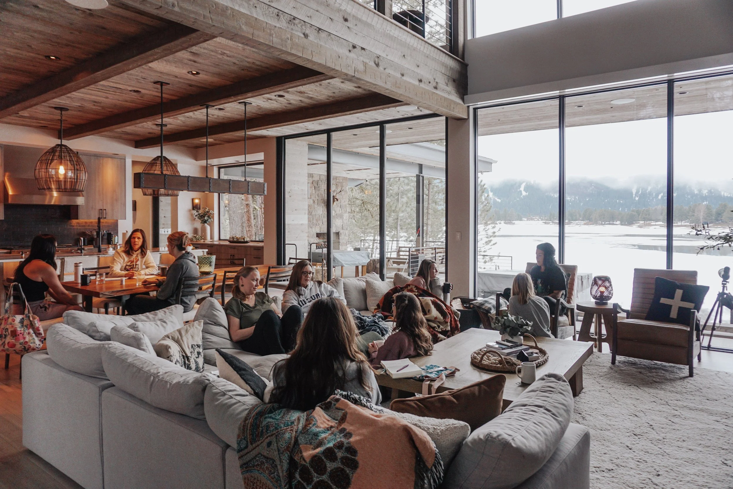 People gathered in a cozy living room with large windows showing a snowy landscape outside, engaged in conversation and relaxing.