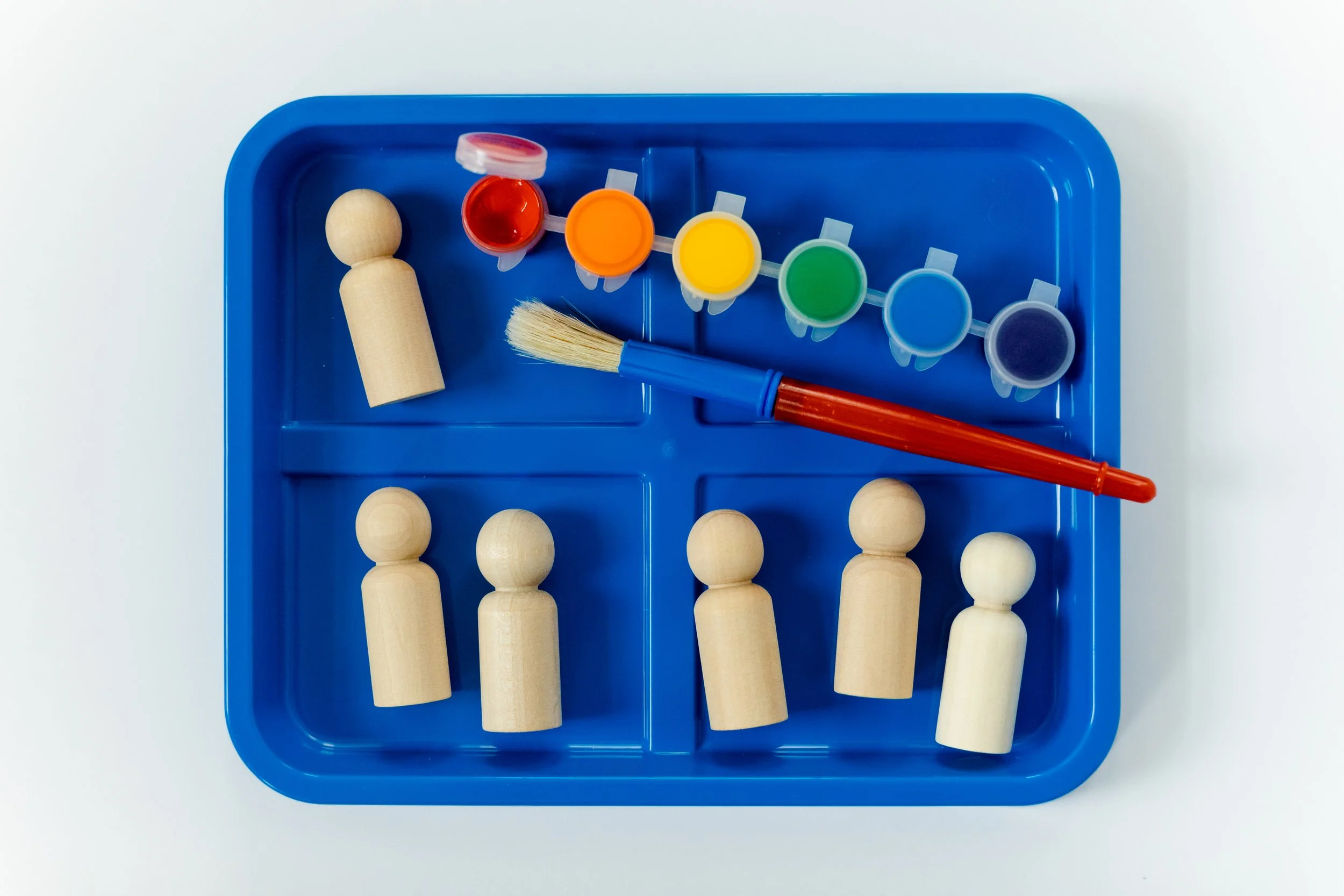 A blue tray with wooden peg dolls, a watercolor paint set, and a paintbrush.