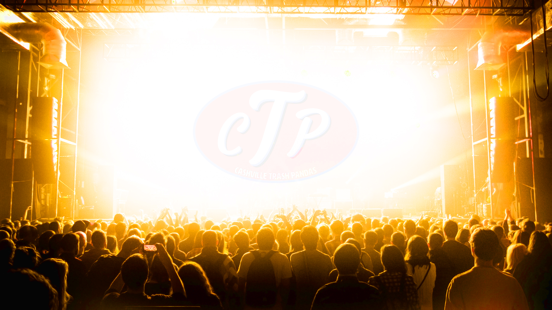 A concert or event with a large crowd facing a brightly lit stage where a logo for Casville Trash Pandas (CTP) is projected, with orange and yellow stage lighting and fans taking photos or videos.
