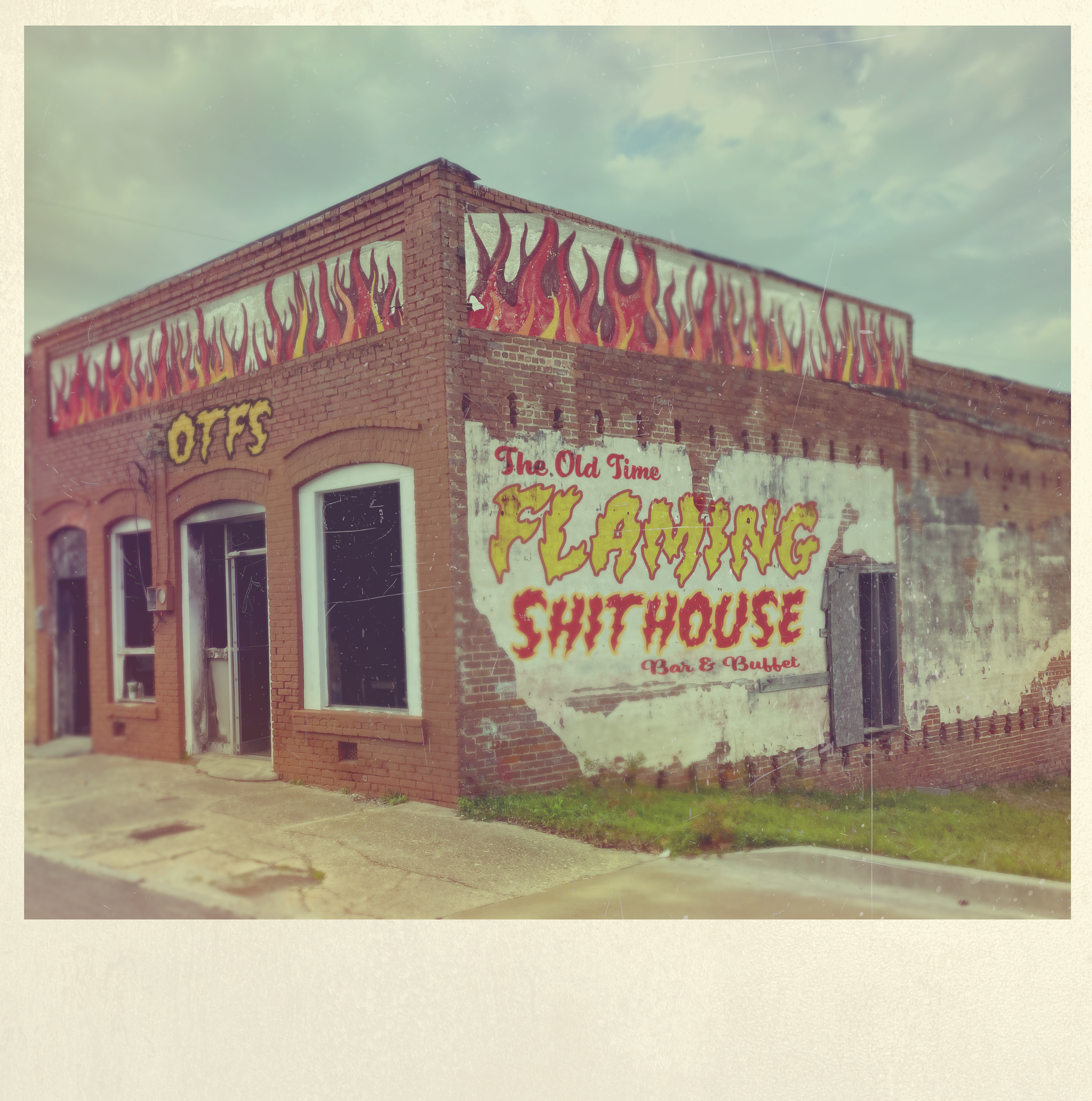 Brick building with colorful billboard painted on the side, advertising a barbecue restaurant called The Old Time Smokehouse Bar & Buffet, with blue sky and clouds in the background.
