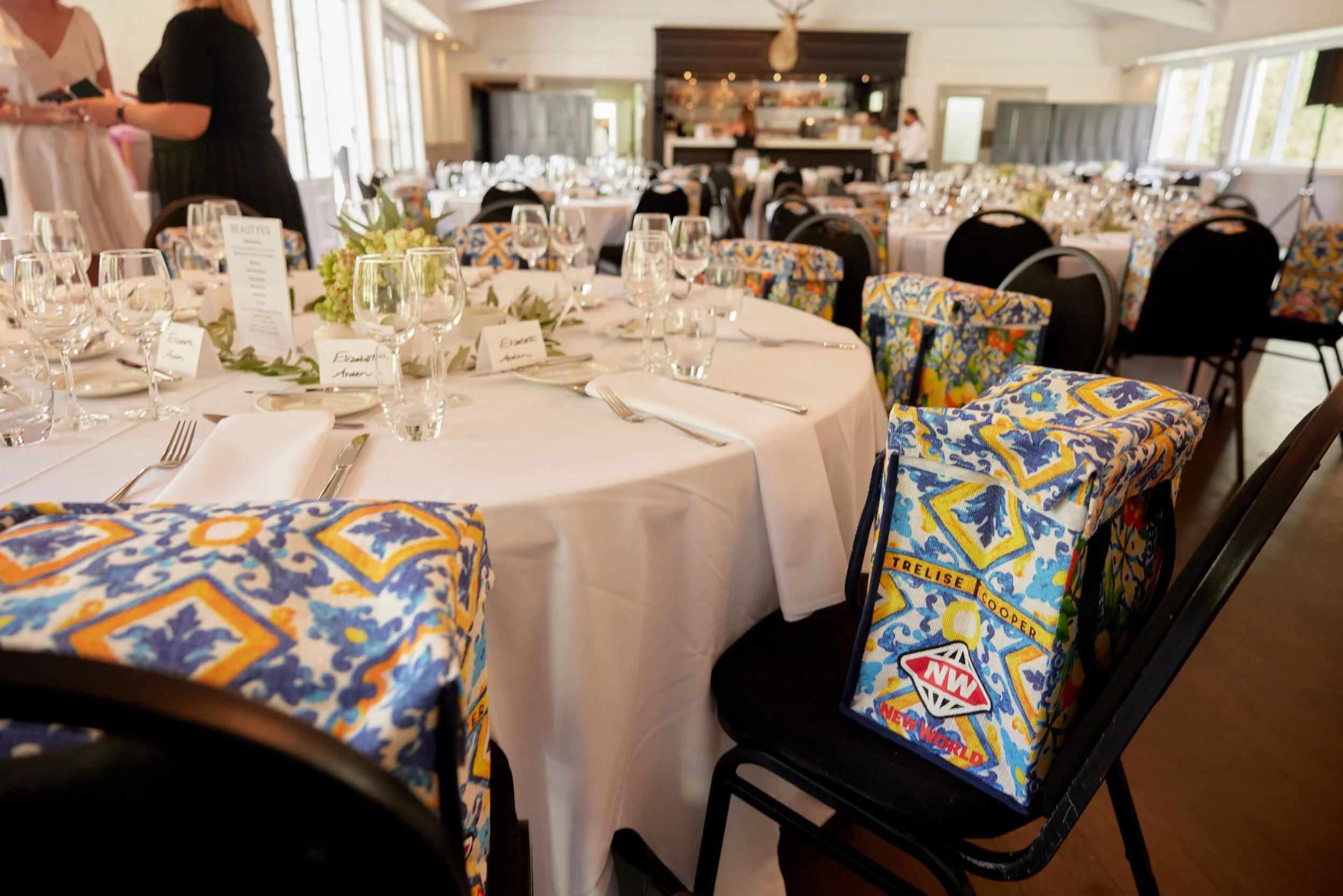 Elegant banquet room set for a wedding or formal event with decorated chairs, white tablecloths, glassware, silverware, and floral centerpieces.
