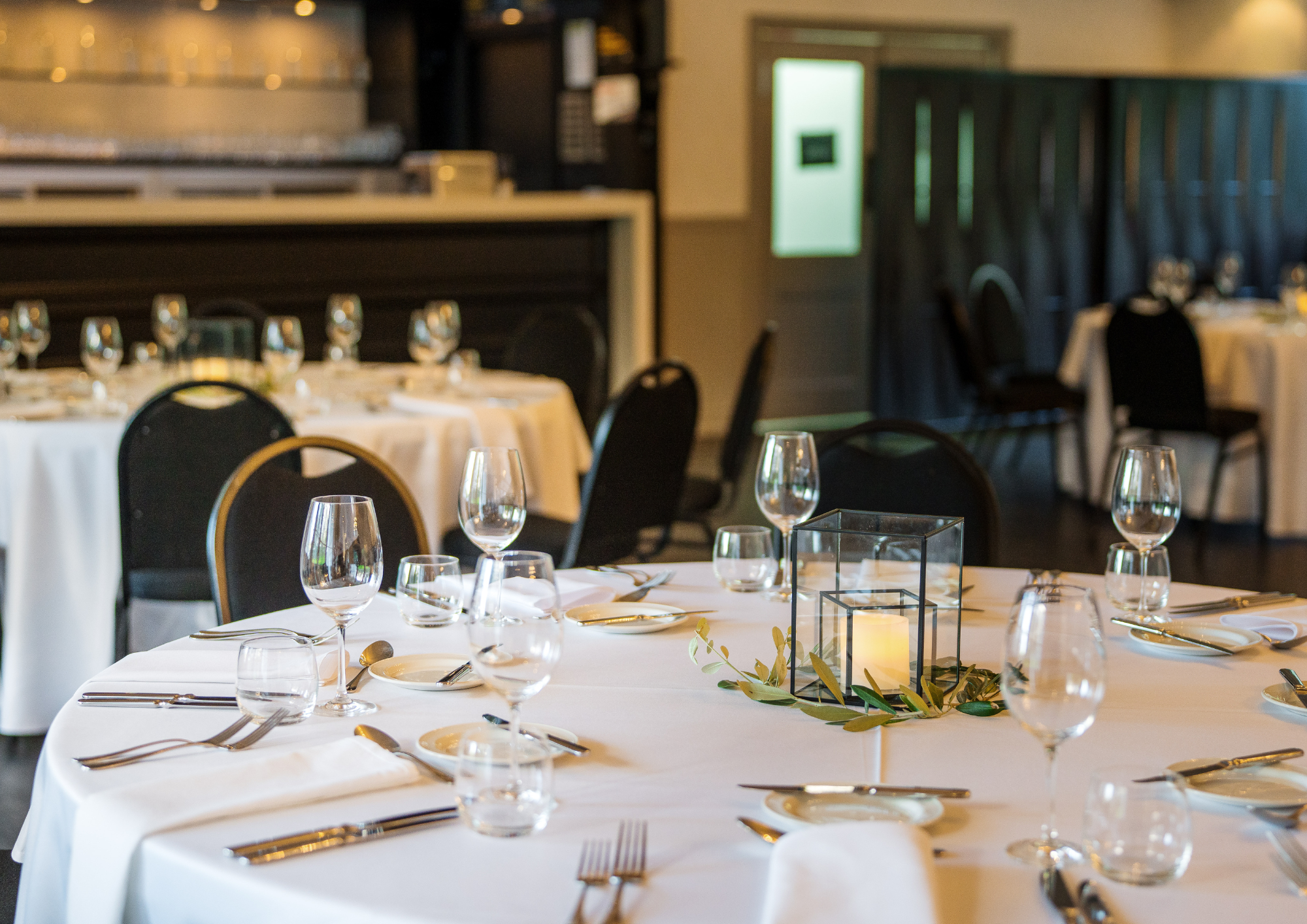 Elegant banquet table with white tablecloth, multiple wine glasses, silverware, small plates, and a decorative candle centerpiece, set in a restaurant dining area.