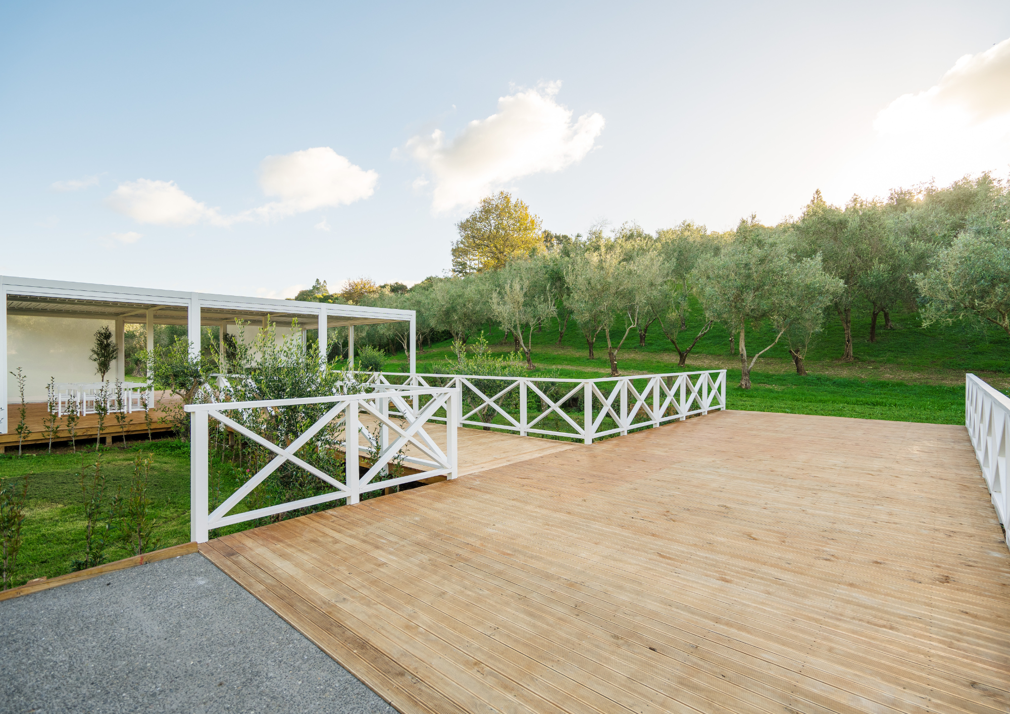 Wooden deck with white railing overlooking a grassy yard with trees and a sunny sky.