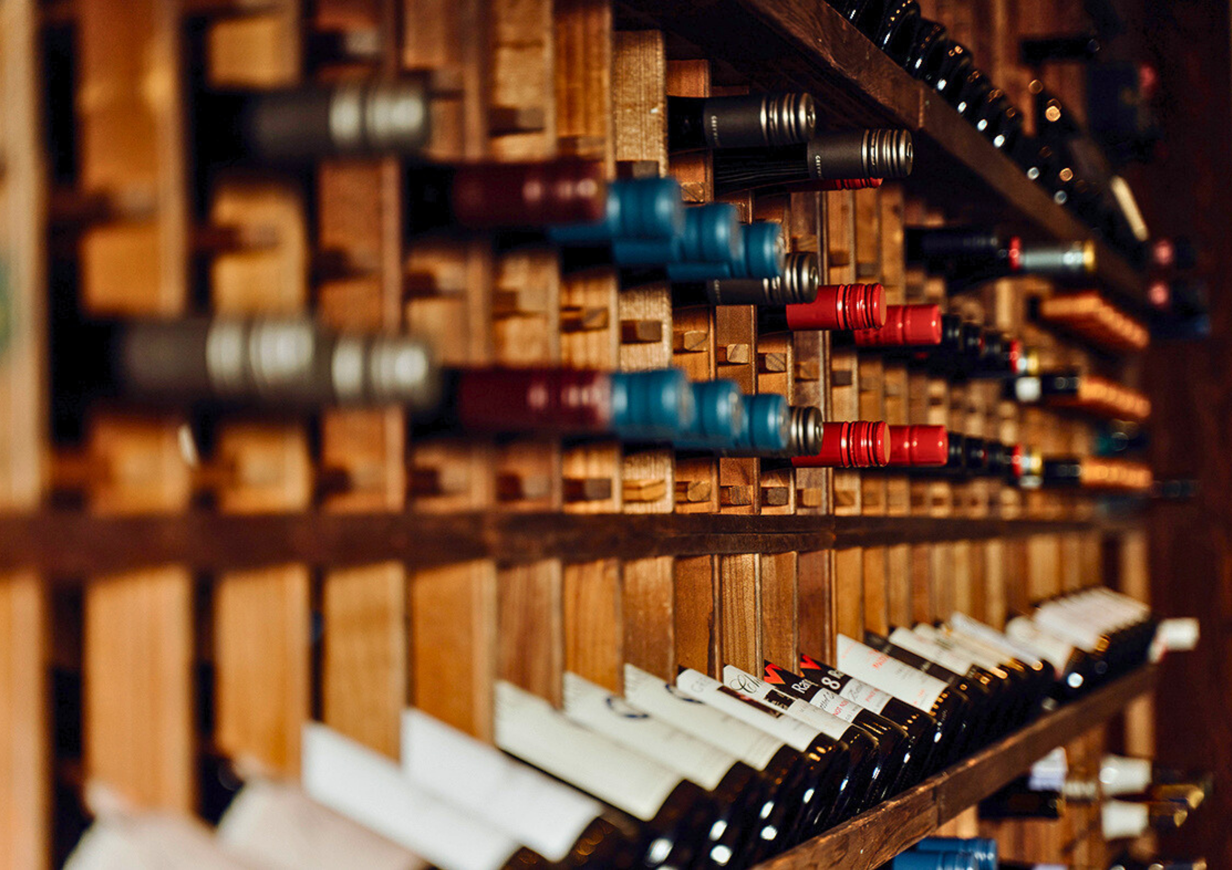 A wooden wine rack filled with various wine bottles arranged horizontally in individual slots.
