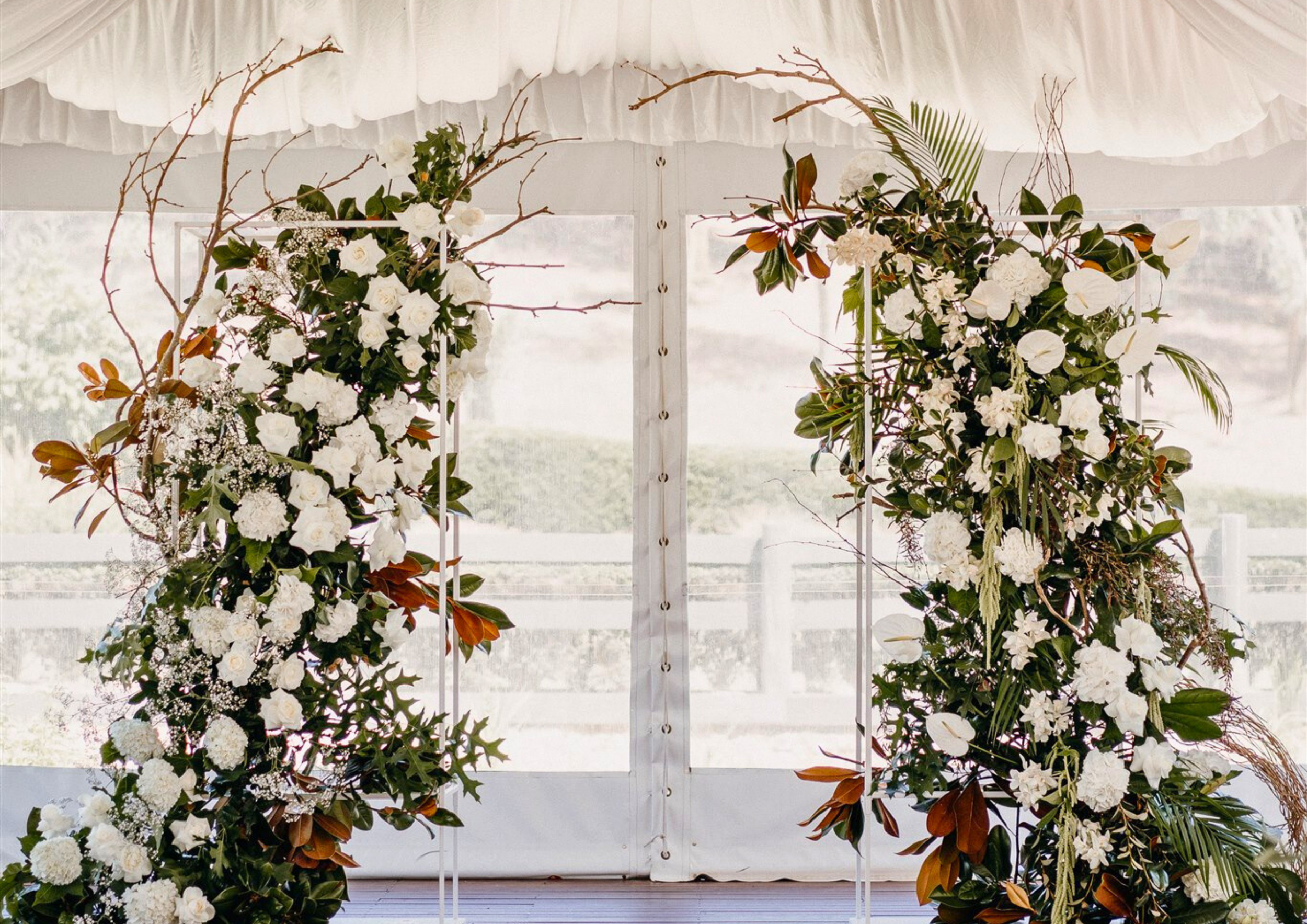 Decorative arch with white flowers and green foliage, set up indoors for a wedding or event.