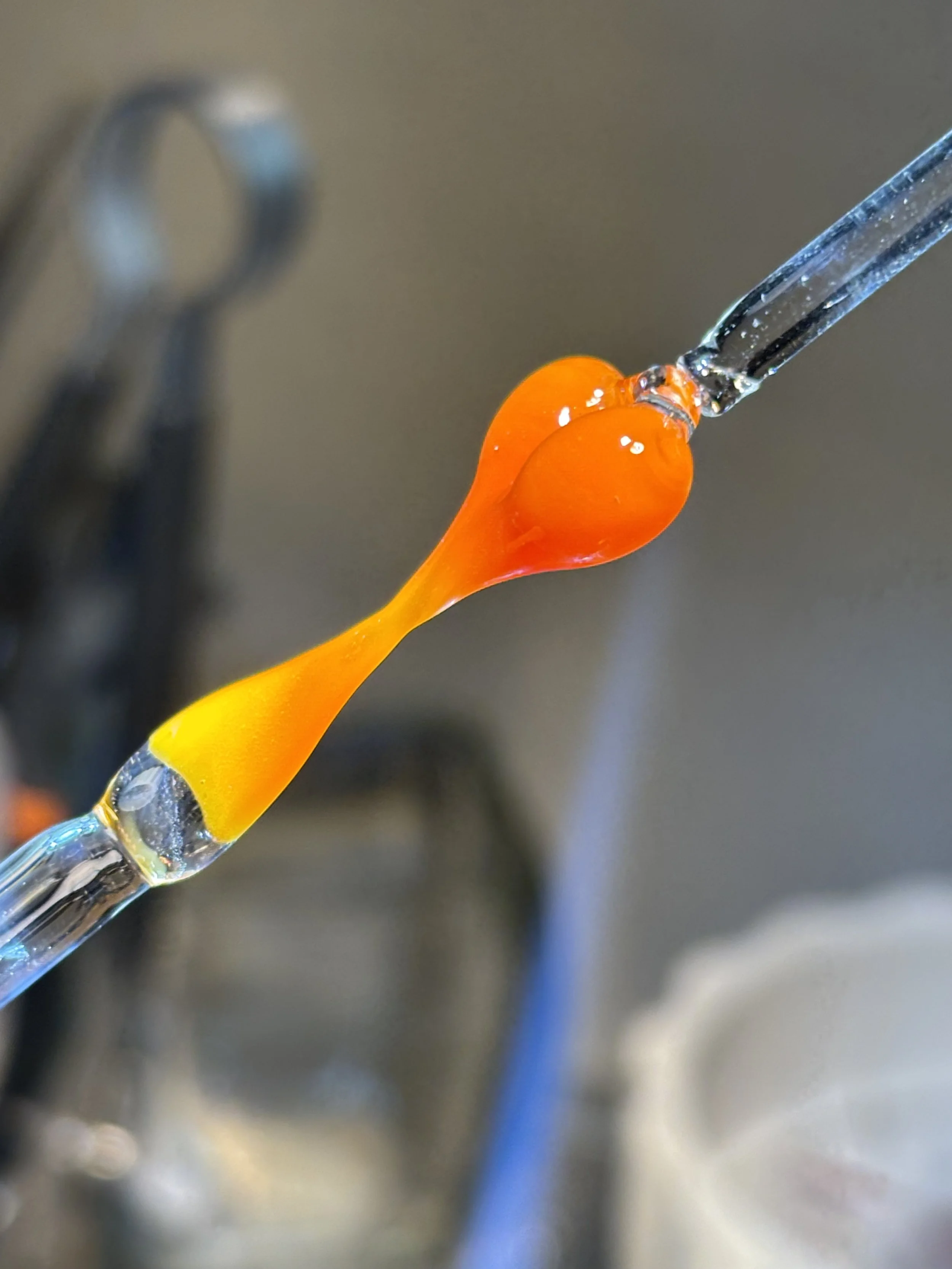 Close-up of orange and yellow glass art piece resembling a droplet or flame, mounted on a glass rod.