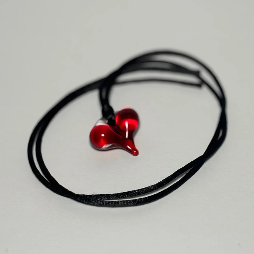 Black fabric necklace with red glass pendant in the shape of a stylized heart or teardrop.