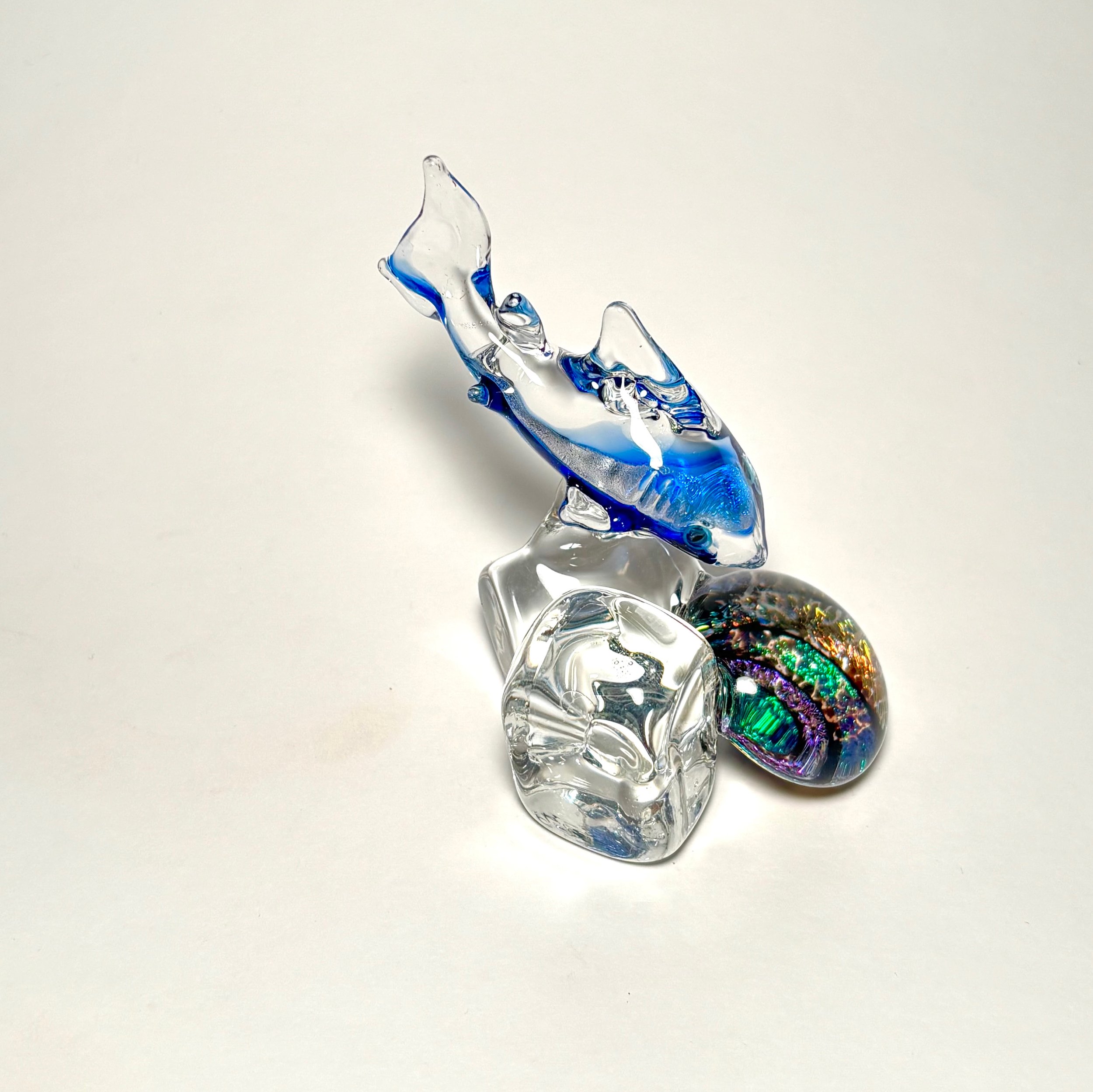 Glass sculpture of a fish, with colorful details, positioned on a white surface.