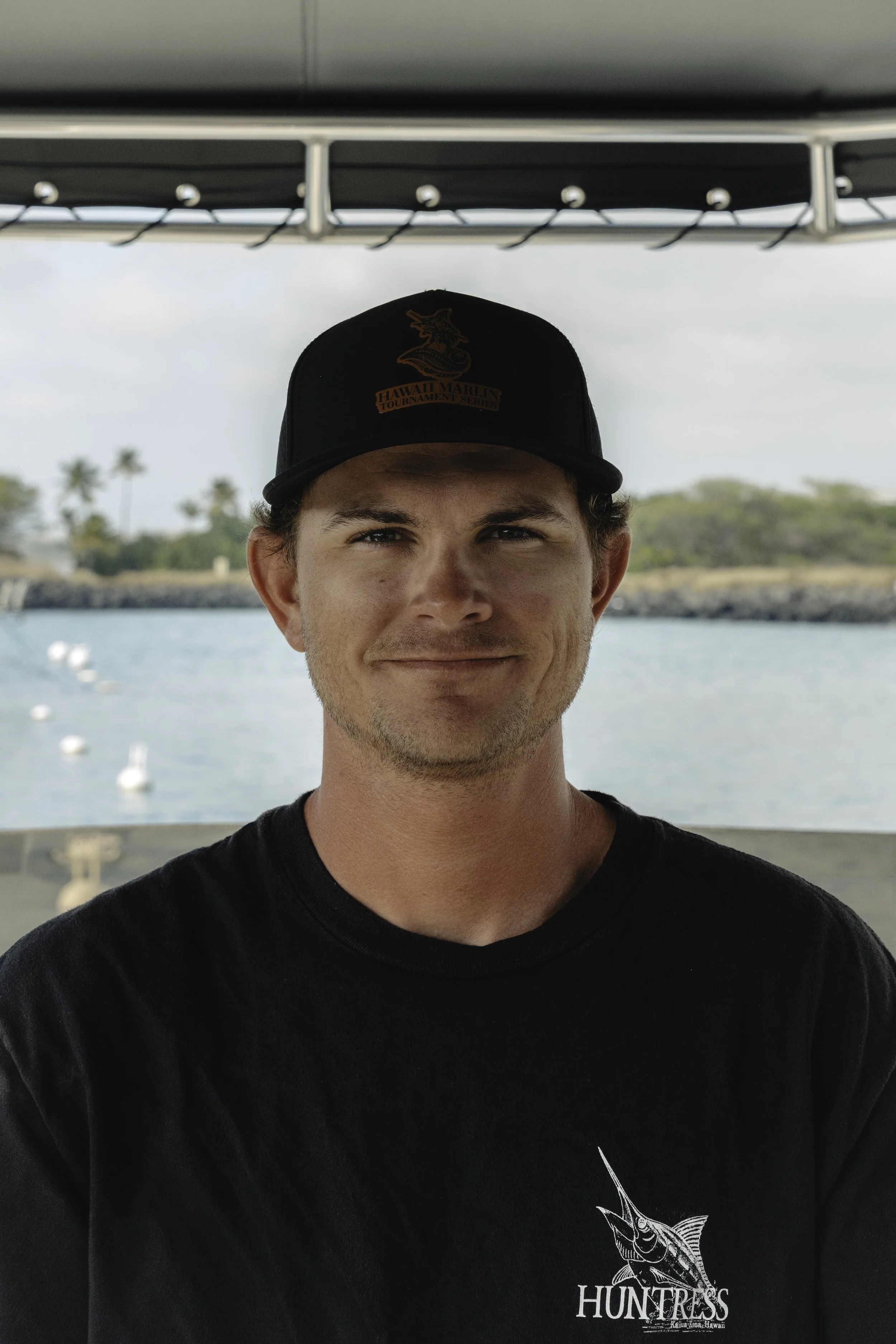 Captain Jack Leverone standing at the helm of a boat, wearing a black Huntress t-shirt and black hat.