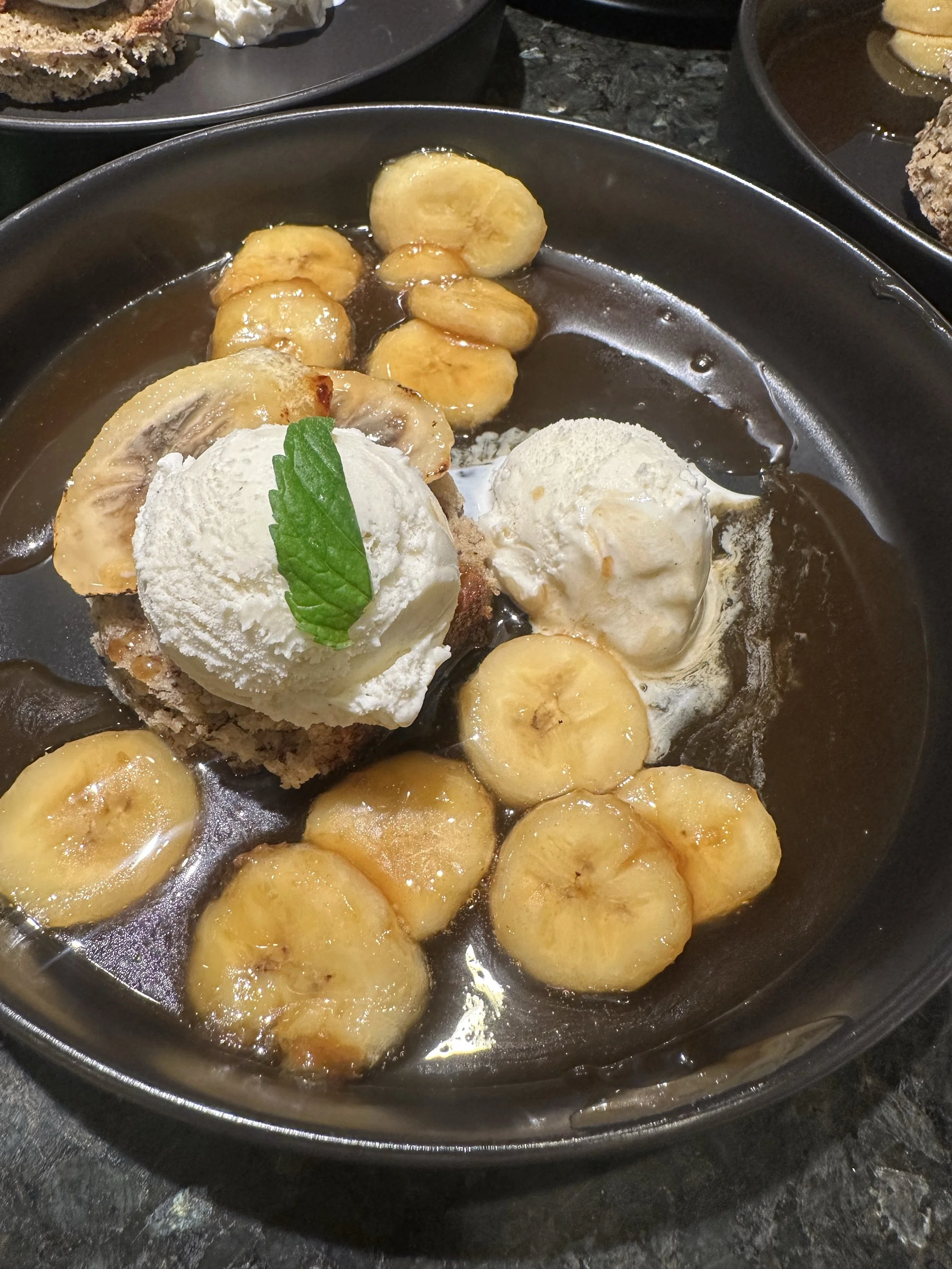 Bananas, ice cream, and a dessert with mint leaf on a black plate