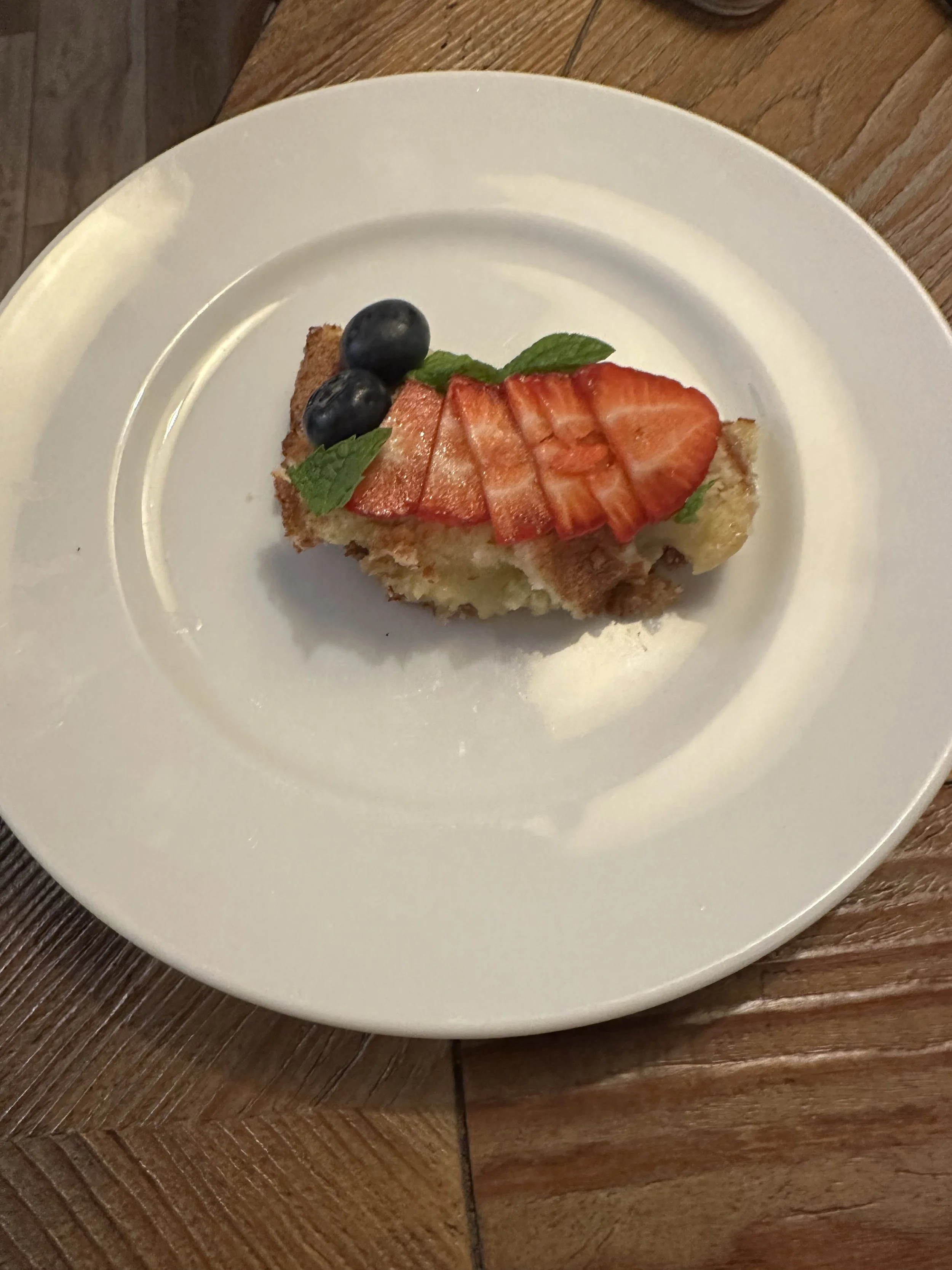 A slice of cake topped with sliced strawberries, blueberries, and mint leaves on a white plate.