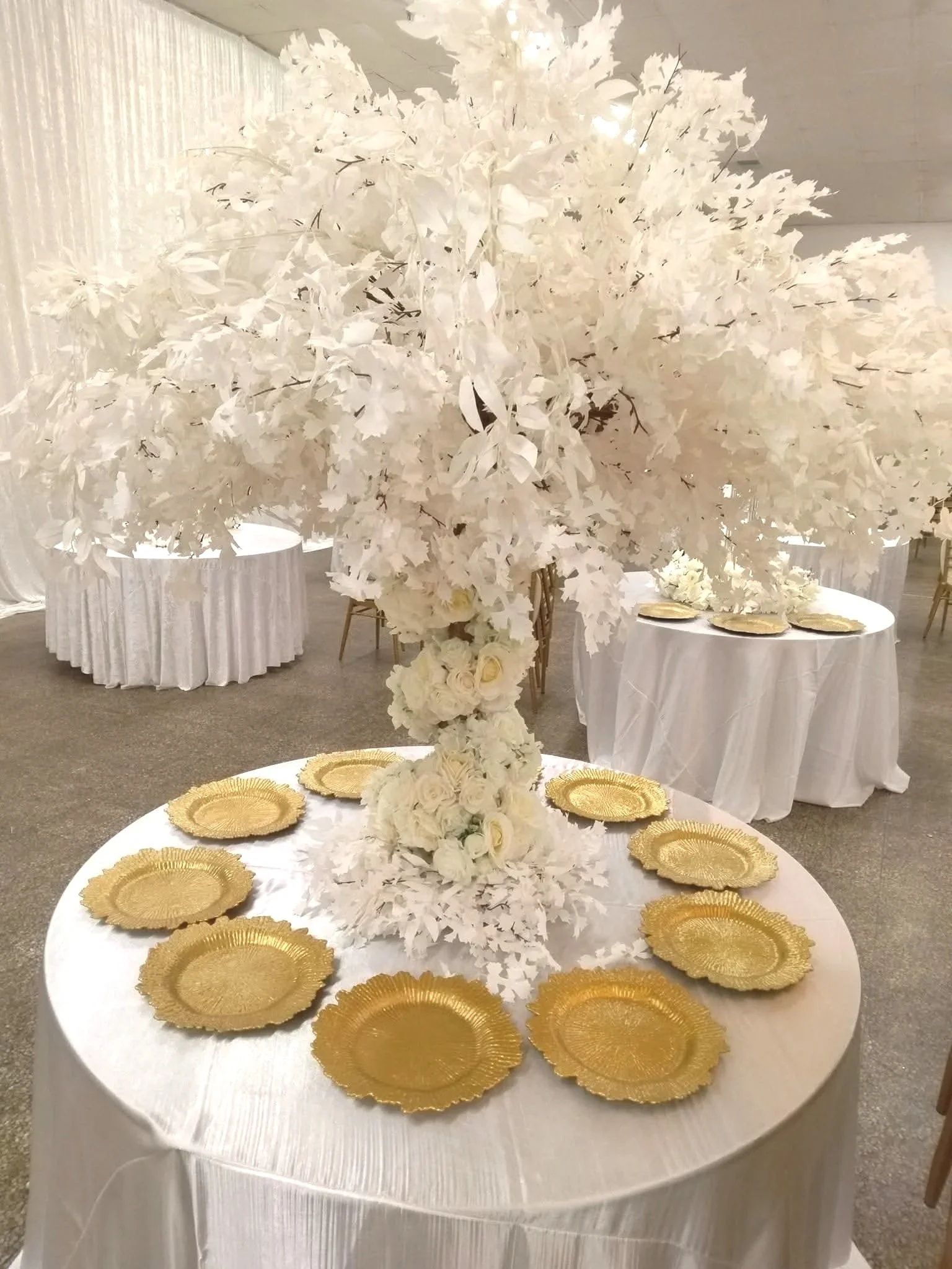 Elegant wedding reception table with a large white floral arrangement centerpiece and gold chargers arranged around the table.