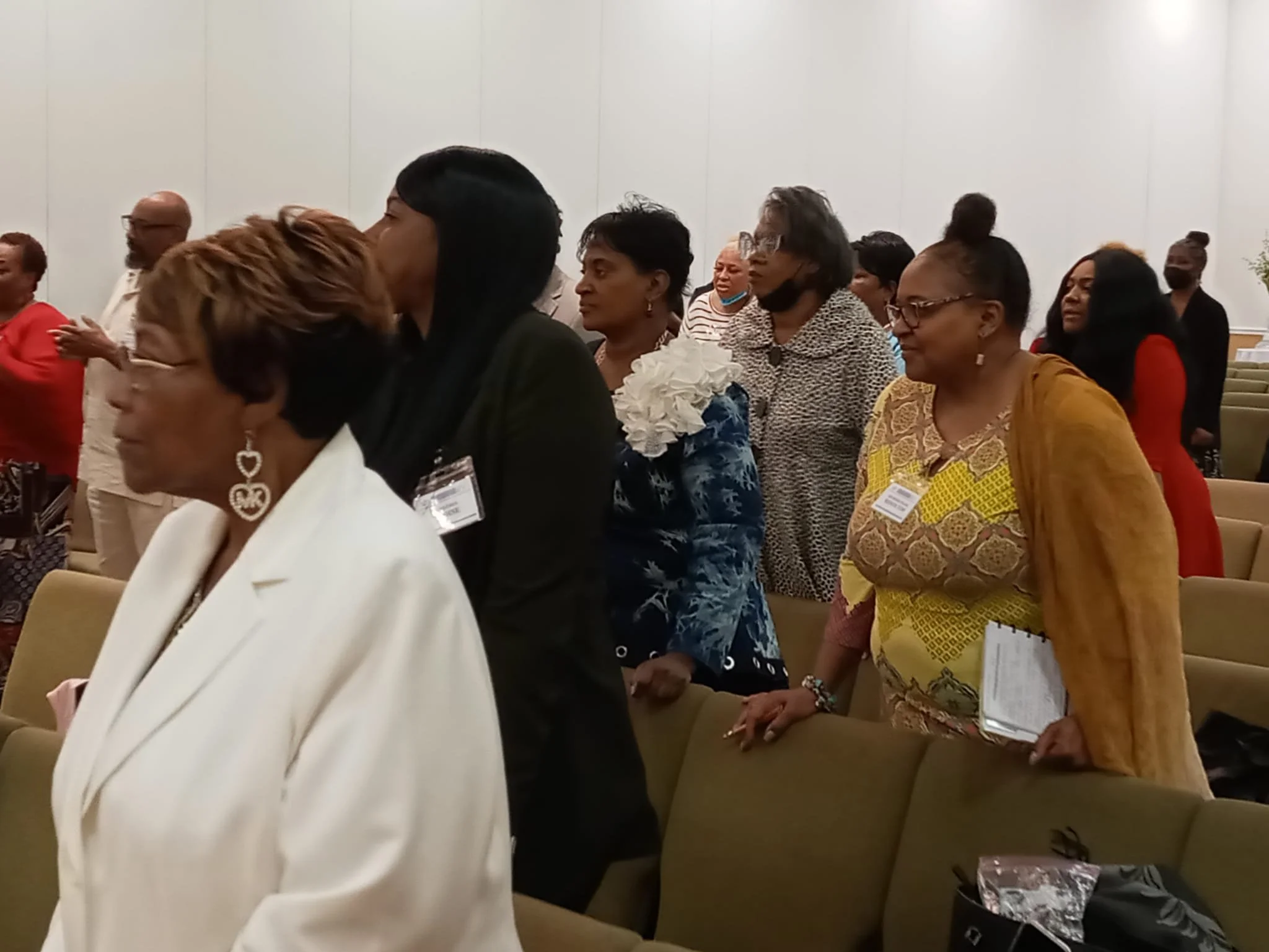 A group of women standing in a church or conference room, many dressed in formal attire, some with name badges, attending a religious or professional event.