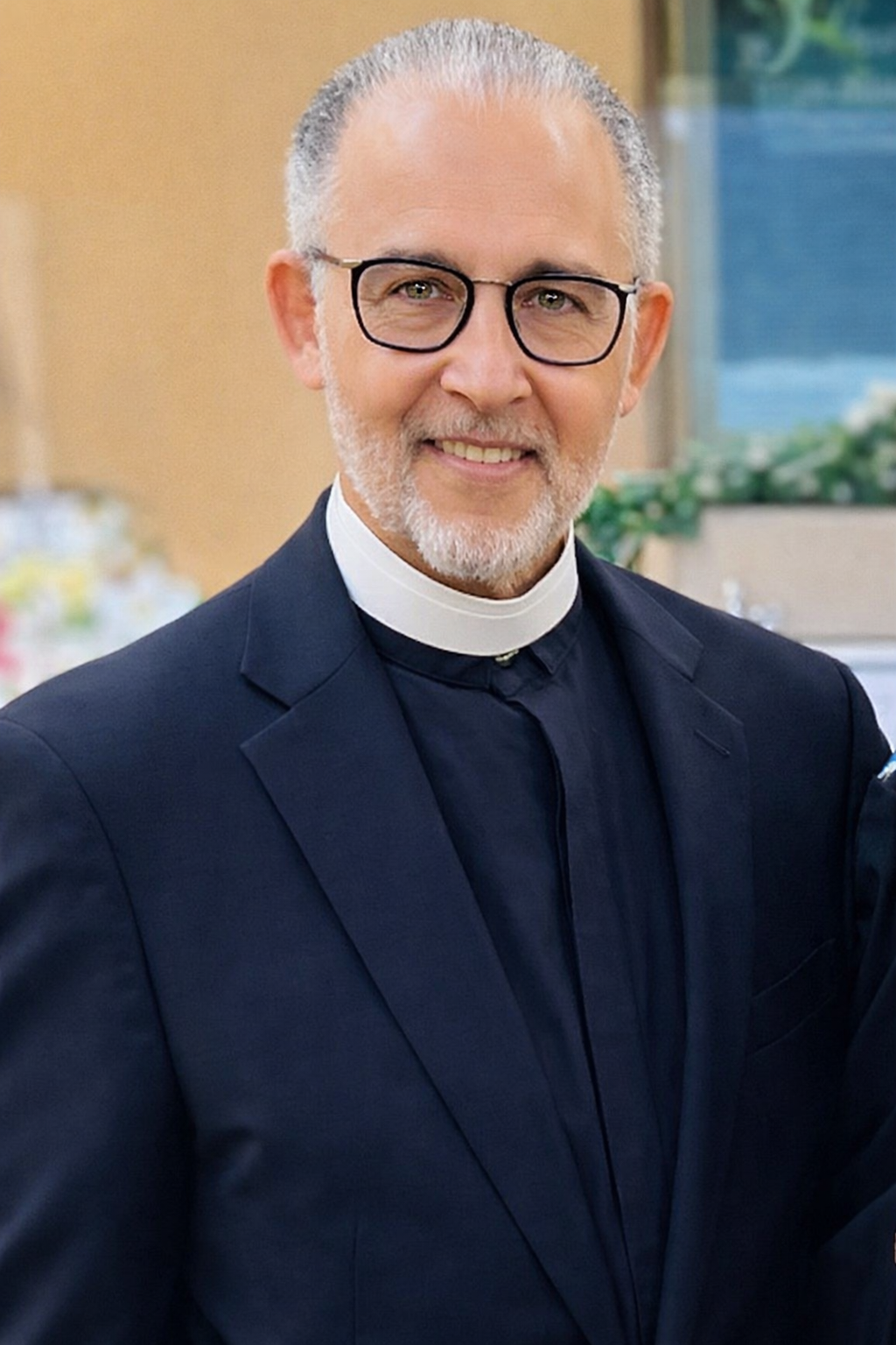 Elder Chester Wortham dressed as a priest, wearing glasses and a clerical collar, standing indoors with a blurred background.
