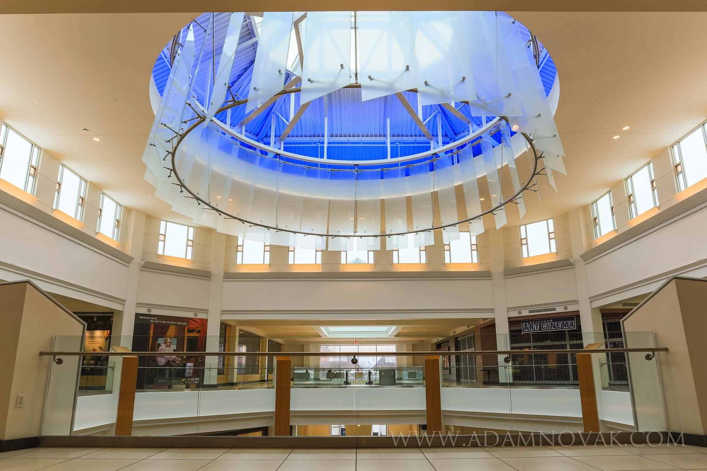 Interior view of a shopping mall with a large circular skylight and modern art installation hanging from the ceiling.