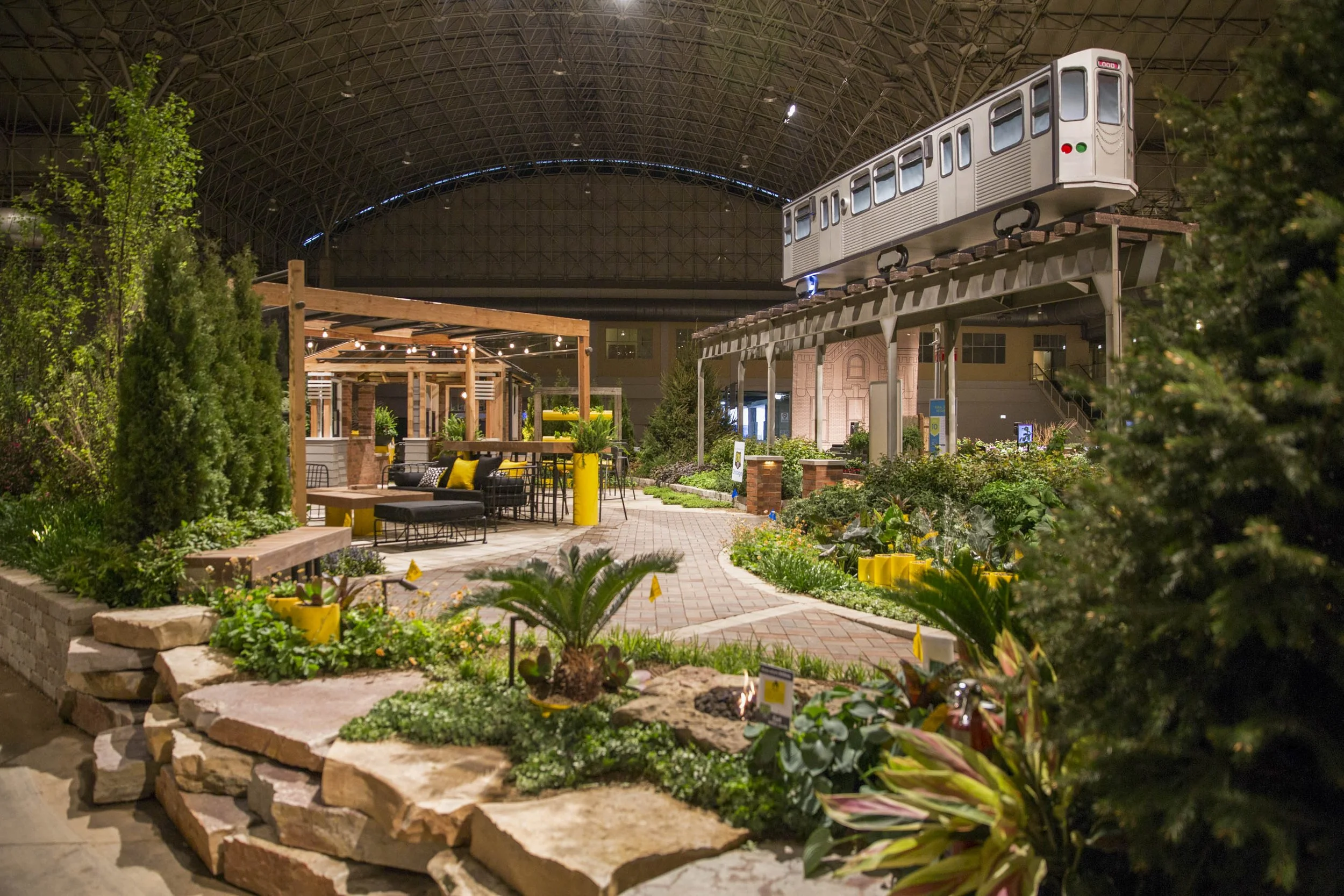 Indoor botanical garden with a vintage train on an elevated track and seating area with string lights.