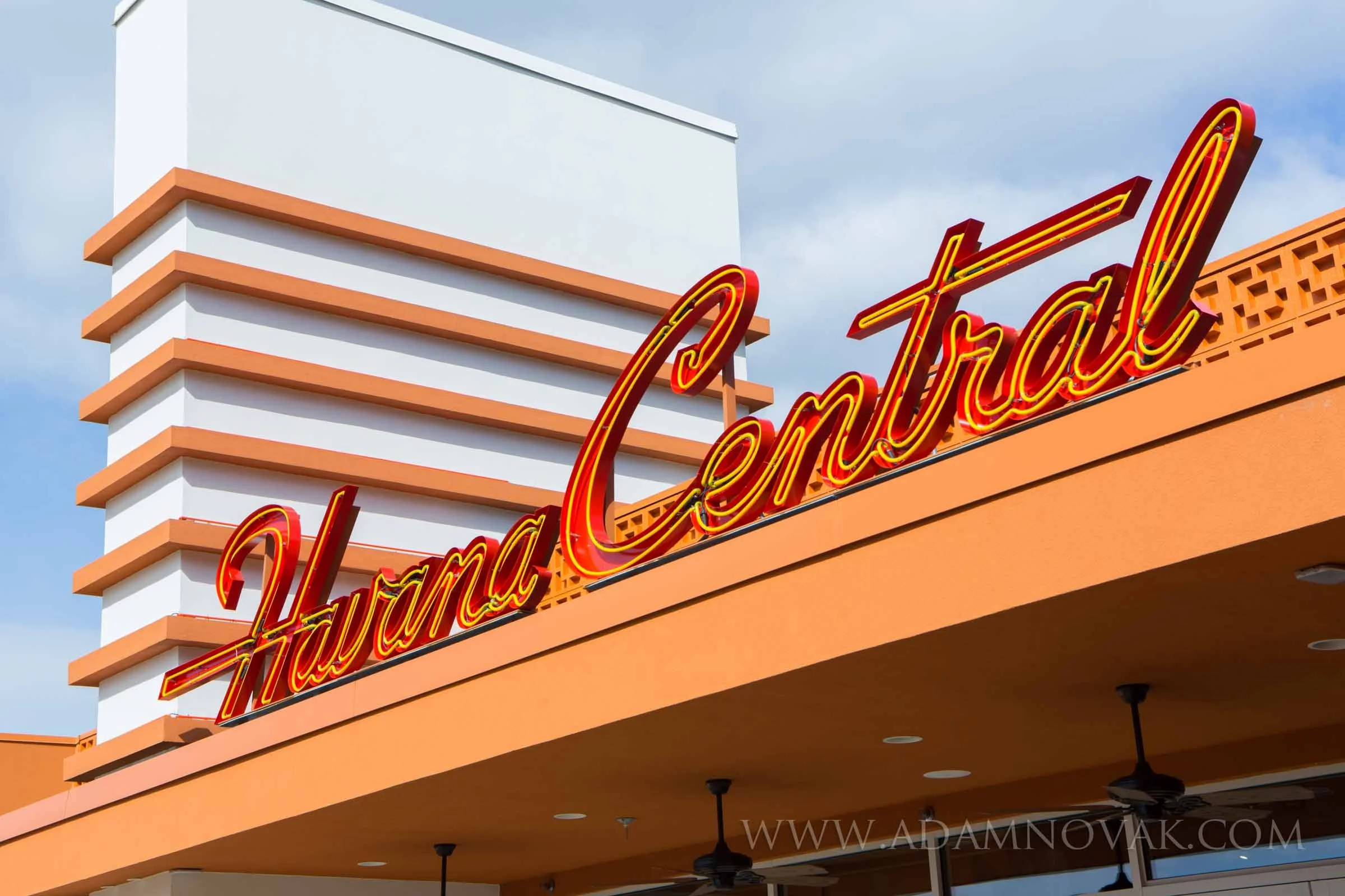 Neon sign reading 'Havana Central' on an orange building facade with a white modern building in the background under a partly cloudy sky.