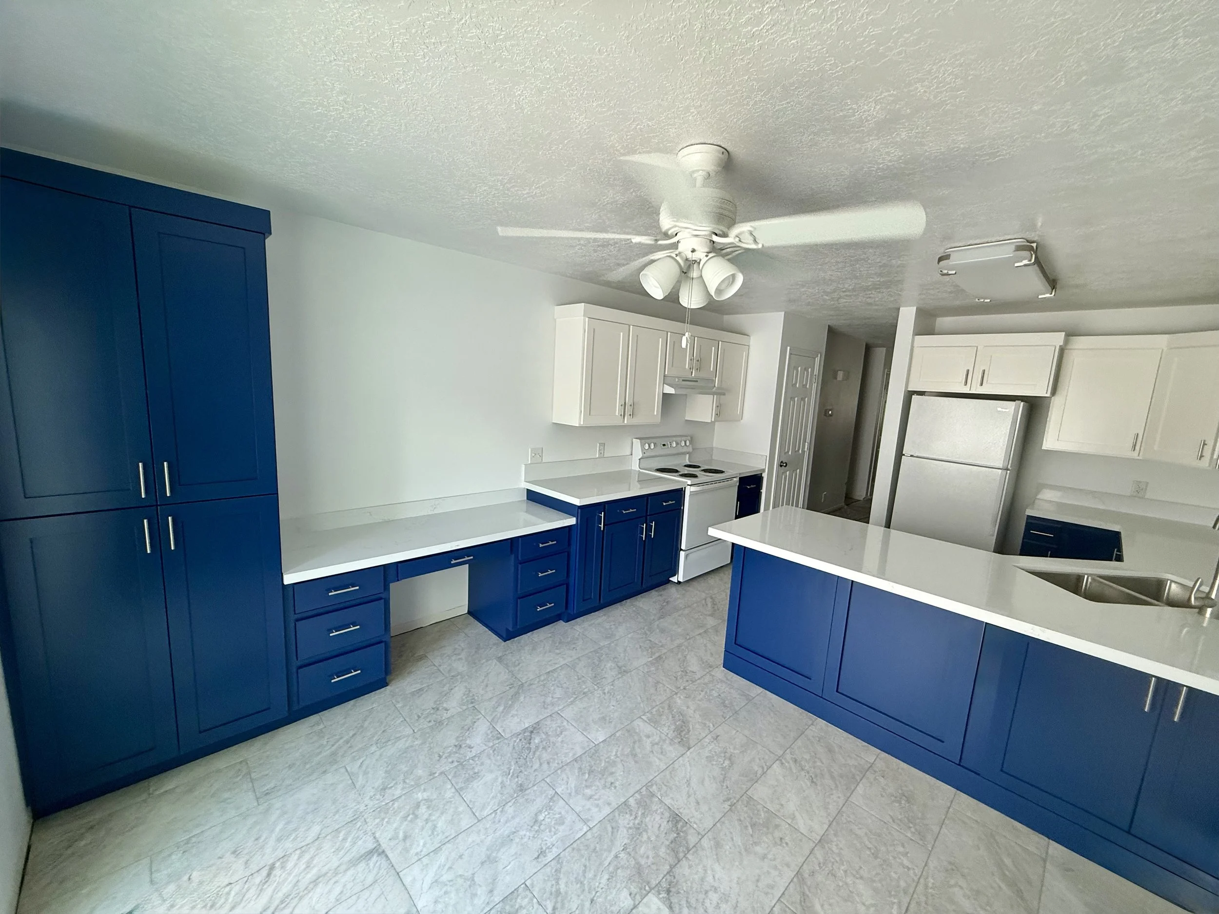 Provo Utah kitchen after cabinet refinishing with navy and white Shaker cabinets, new crown molding, trim, custom cabinetry, and quartz countertops