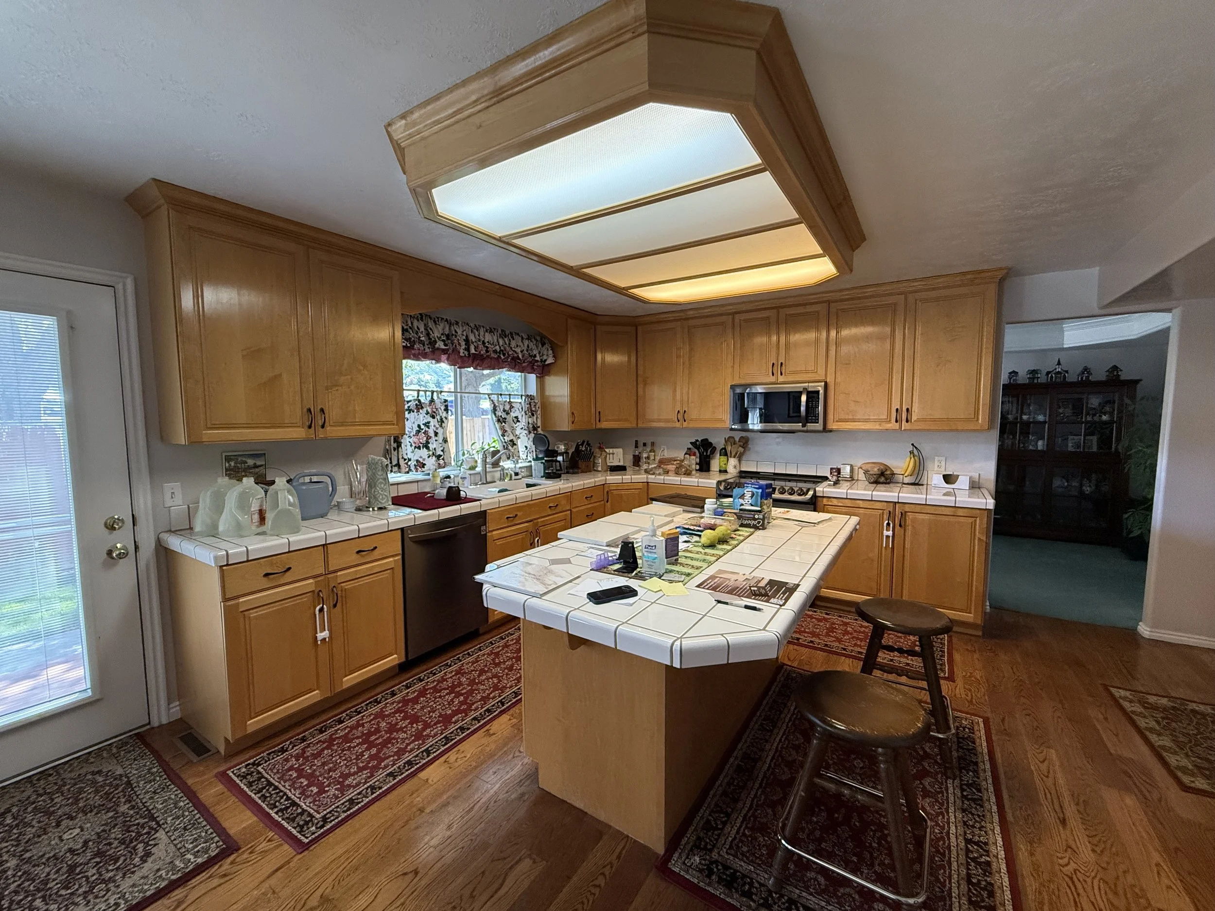 BEFORE | Original wood cabinetry with raised-panel doors and dated tile countertops.