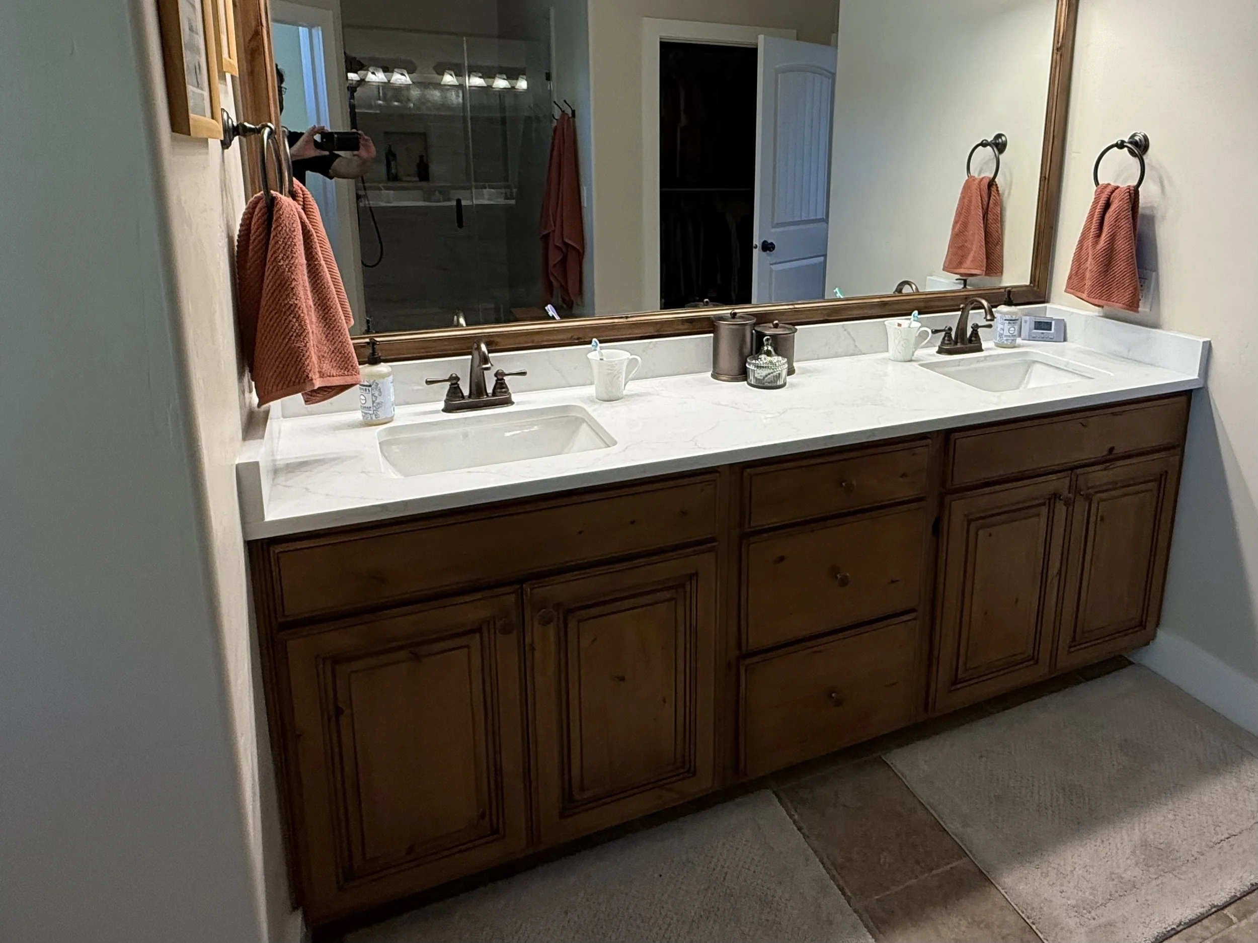 AFTER | Pleasant Grove, Utah bathroom vanity after professional cabinet refinishing and restaining by CAZI Refined Finishes, featuring a richer wood finish, refinished mirror frame, and updated white countertop with undermount sinks.