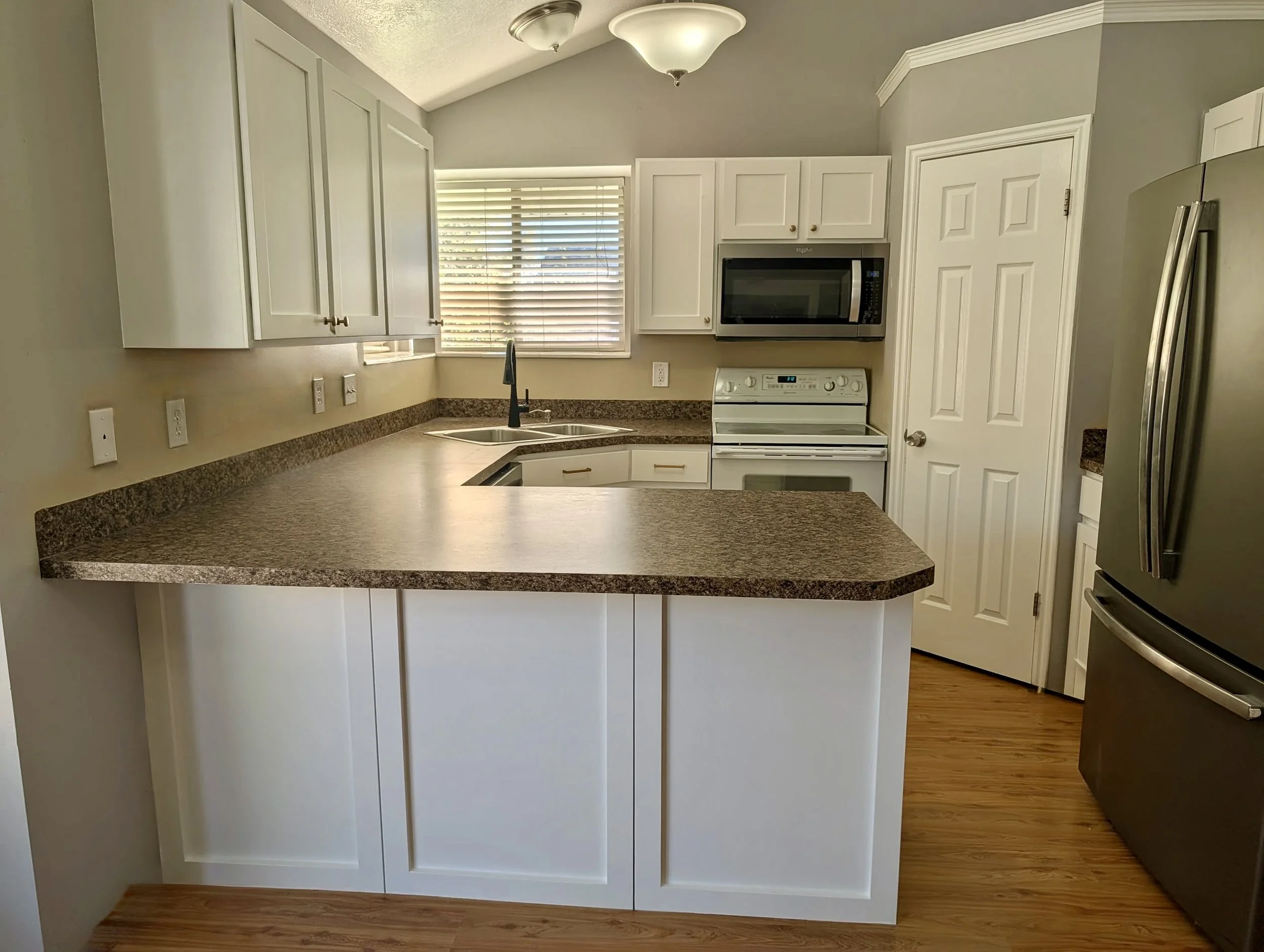 Layton, Utah kitchen after cabinet refacing by CAZI Refined Finishes, featuring new Shaker-style cabinet doors, flat drawer fronts, and decorative peninsula trim while retaining the existing cabinetry.